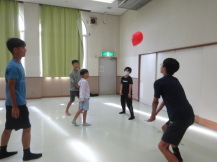 5名の参加者のうちの1名が落ちてくる赤い風船をレシーブの姿勢で打とうとしている写真