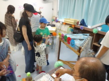 「だがしくじ」と書いた紙が貼られたくじ台の前で来場者の子どもが1本のくじがついた糸を引っ張っている様子を関係者が見守っている写真