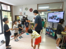 4名が1列に立って並び、その前で関係者が話をしている様子の写真