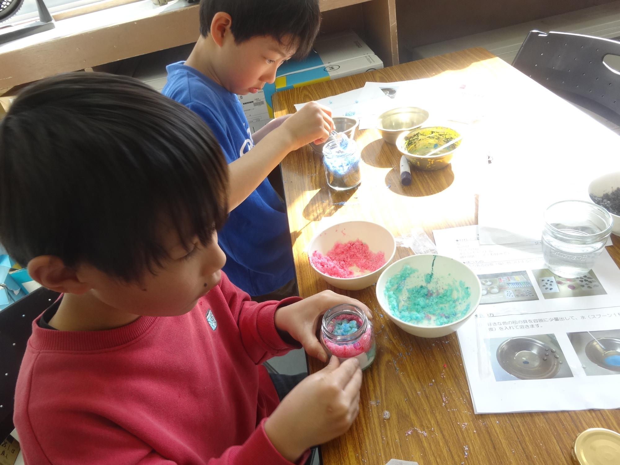 色を付けた塩をビンに詰め、模様をつけている小学生の写真