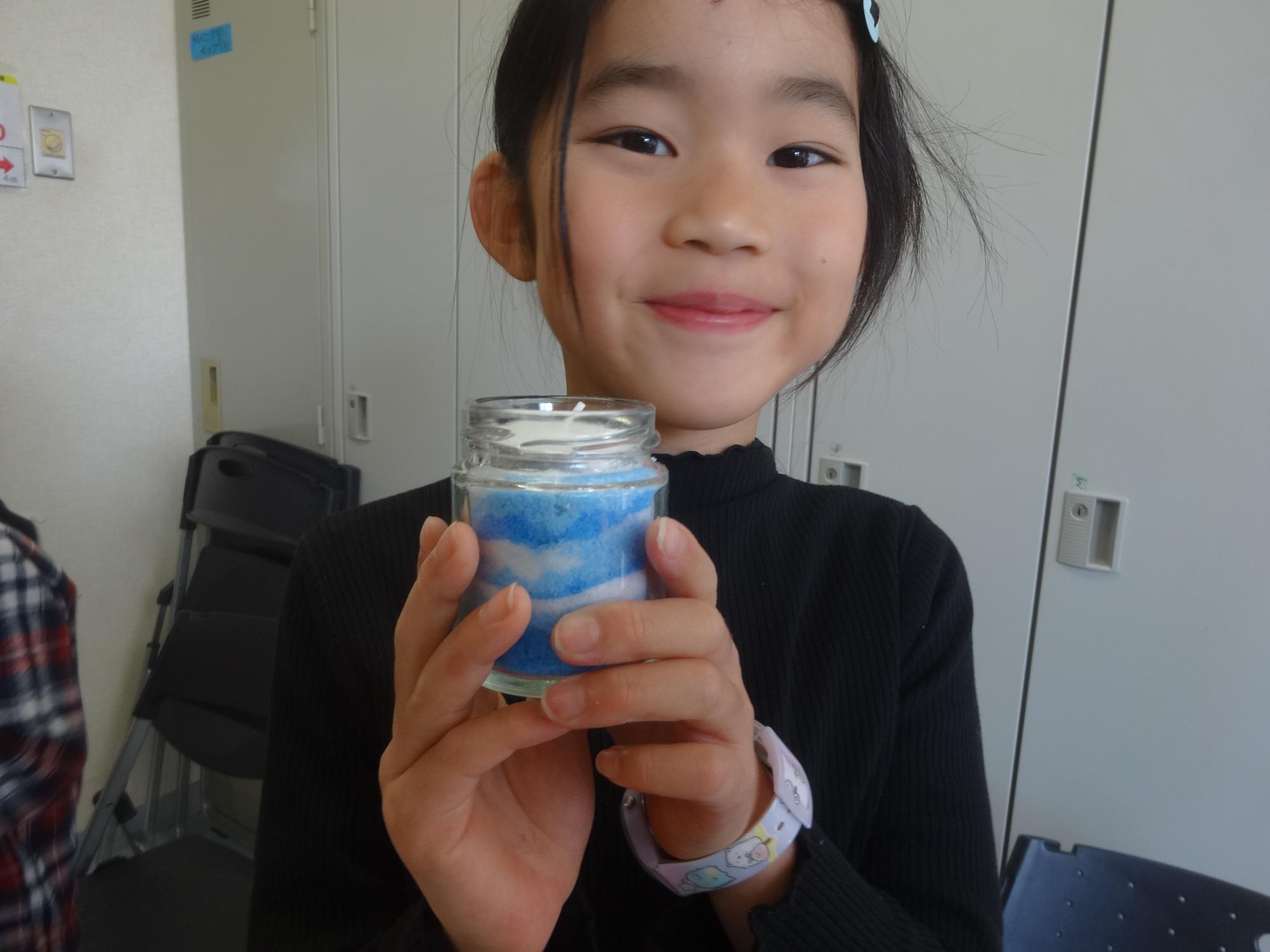 完成したキャンドルホルダーを手に微笑む小学生の写真