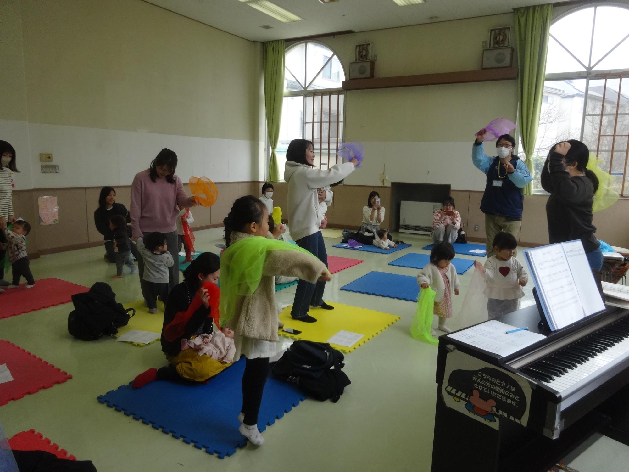 色んな音に合わせて、何色もの布を振っている幼児親子の写真