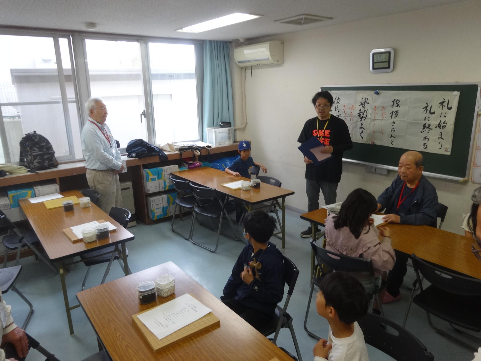 囲碁の先生方と小学生の前で挨拶をする館長の写真