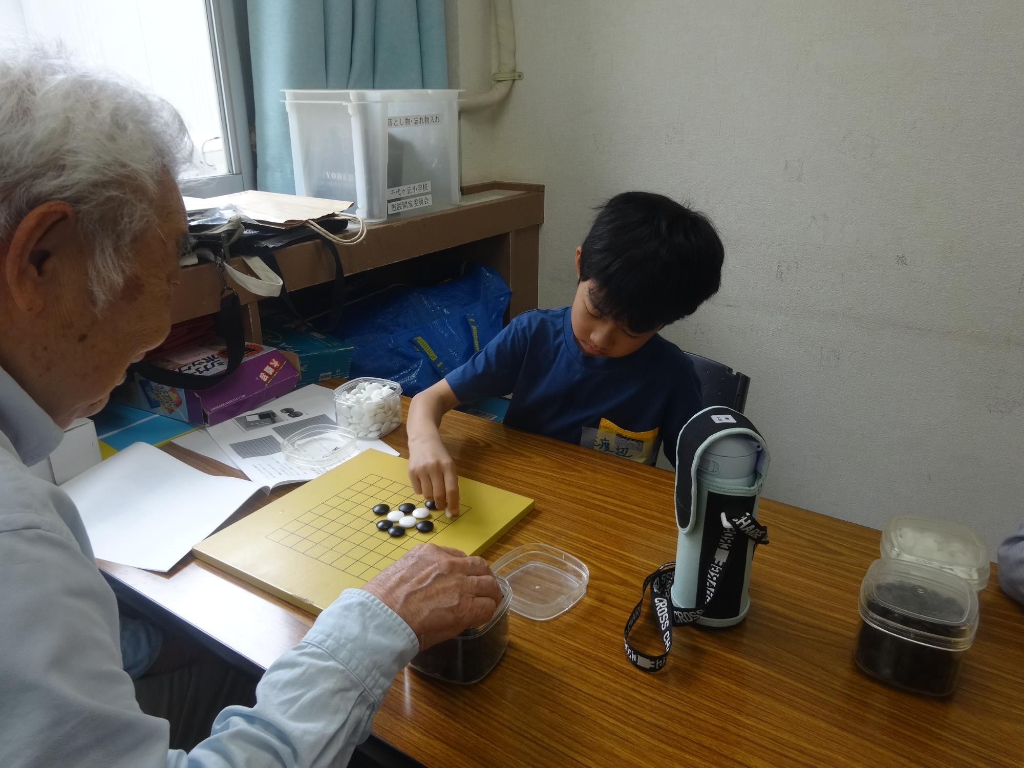 先生と囲碁の対局をしながらルールを学んでいる小学生の写真