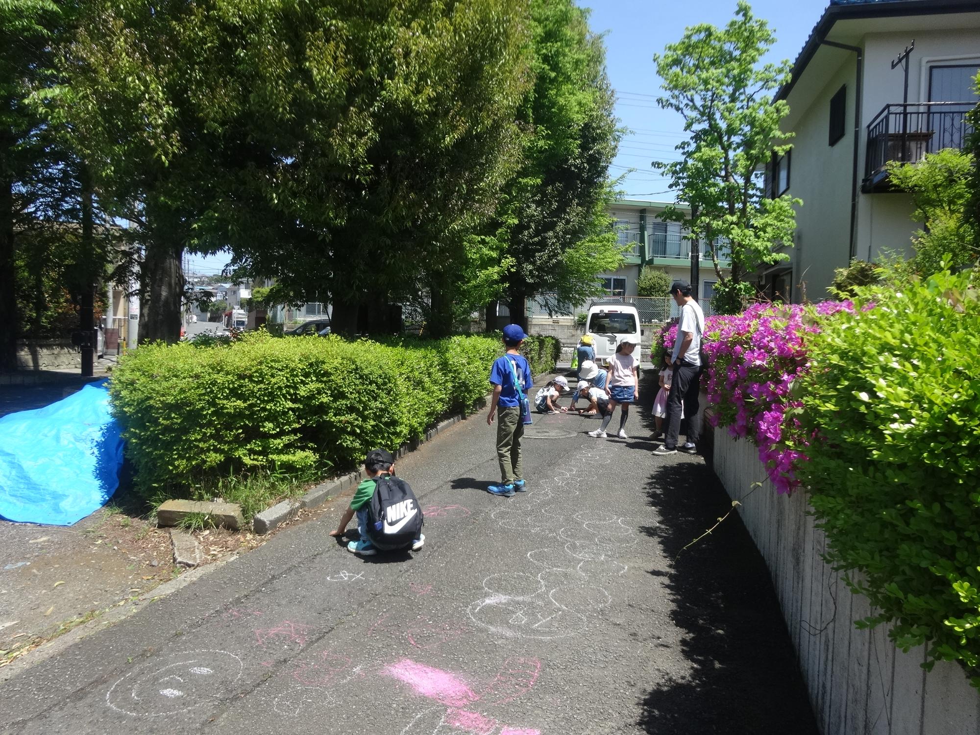 青空の下でチョークで絵を描くファミリーと小学生たち