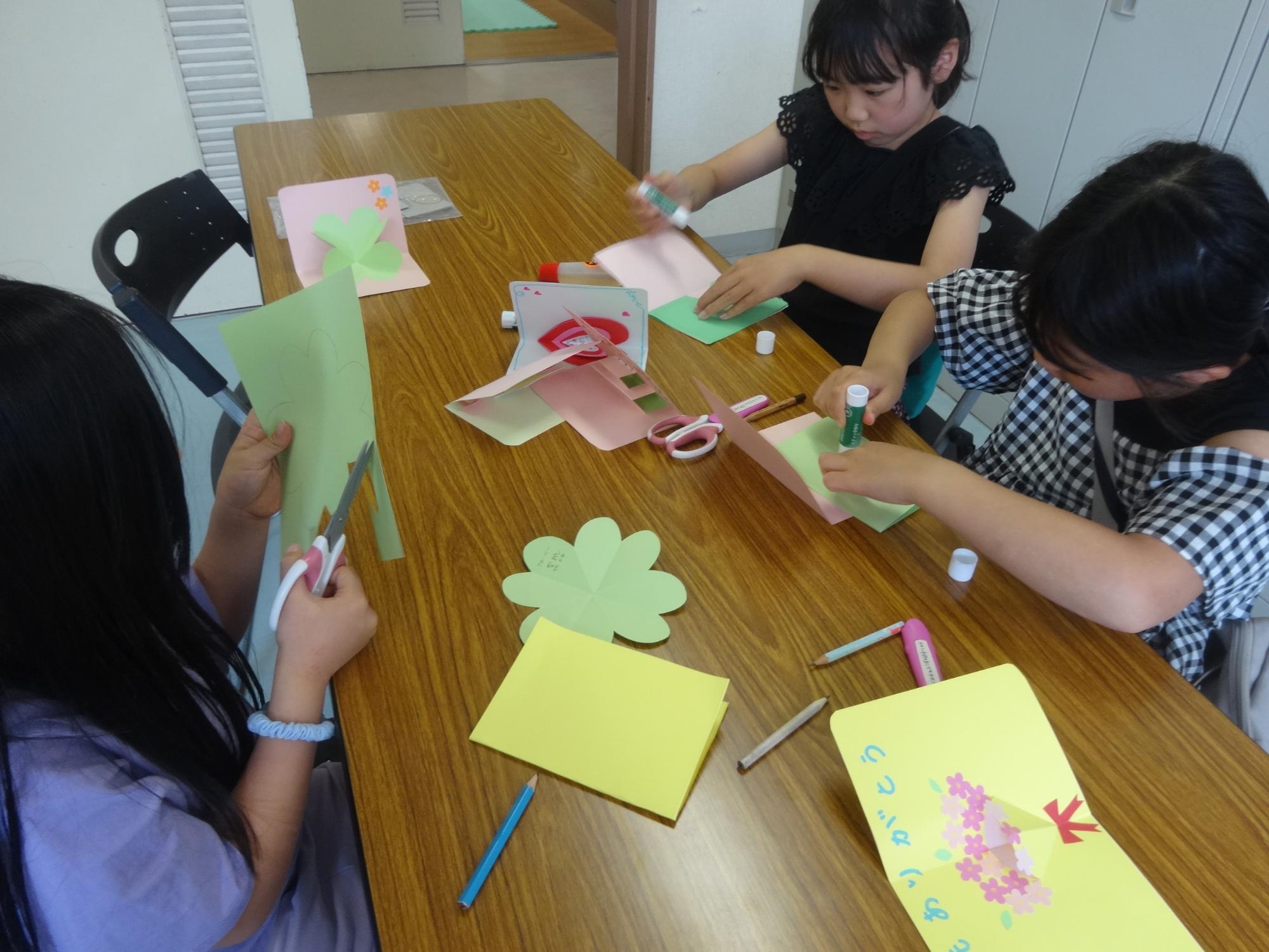 紙を切ったり、のりで貼ってカードを作る小学生