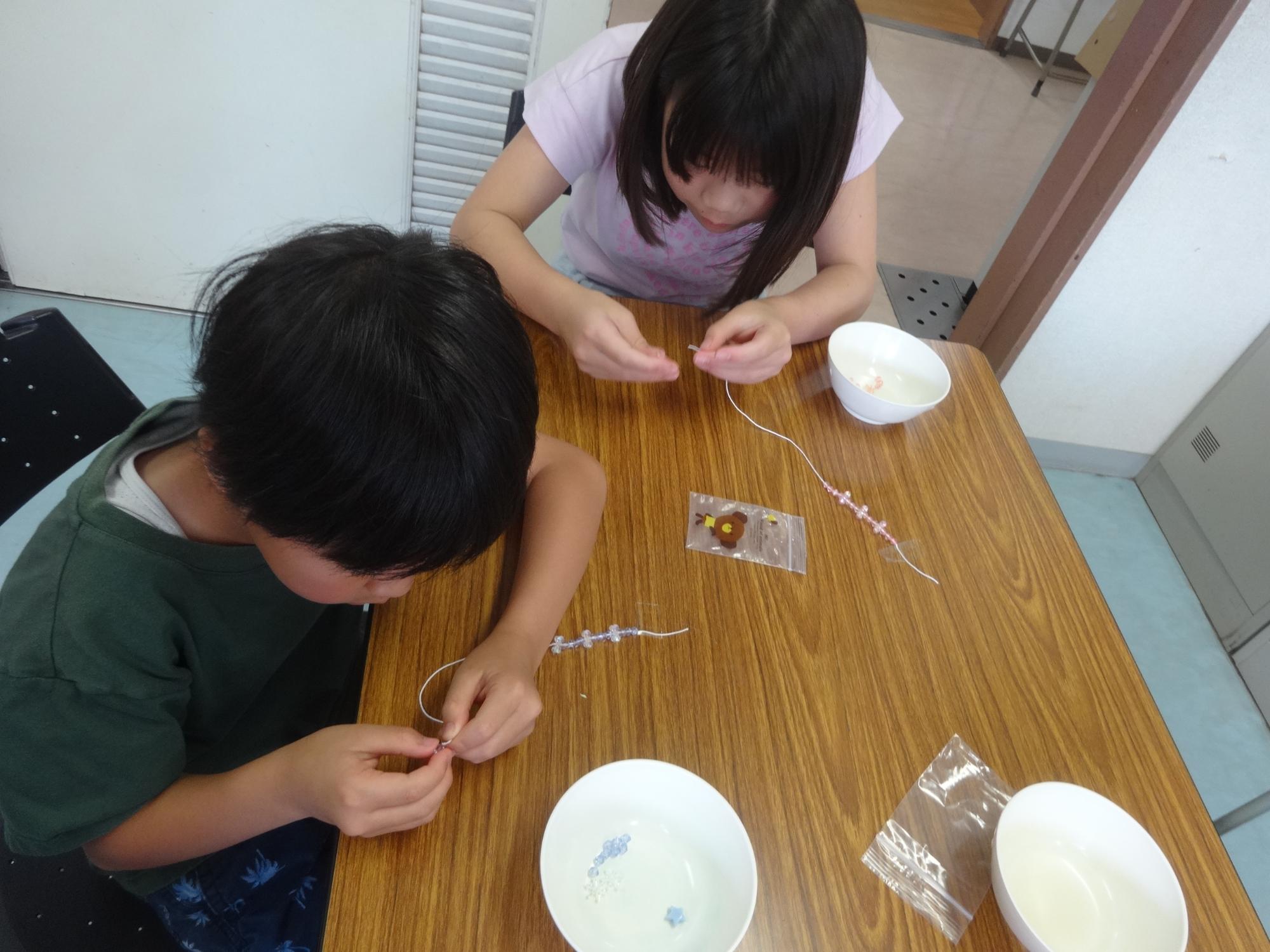ビーズを糸に通してストラップを作る二人の小学生