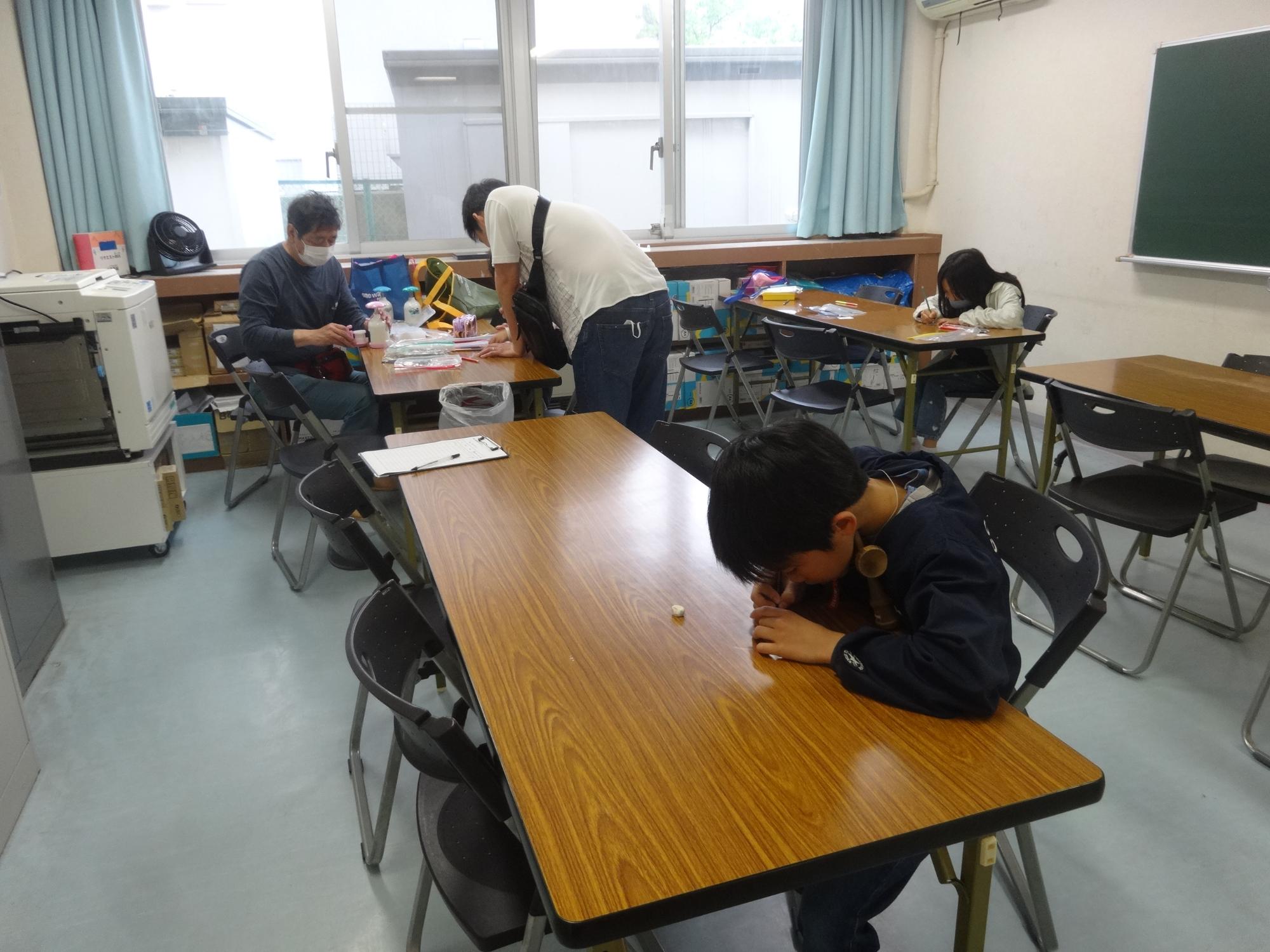 缶バッジのデザインを考えて絵を描く子どもたちと講師の先生の写真