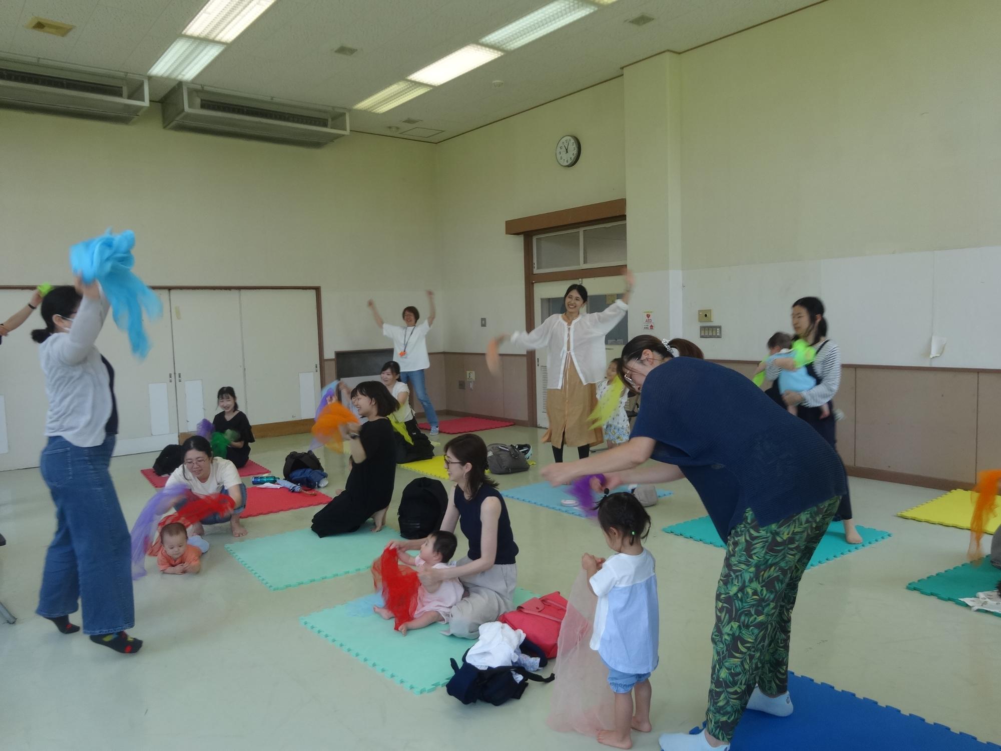 講師の先生の掛け声に合わせてダイナミックに体を動かして遊ぶ赤ちゃんとお母さんたち