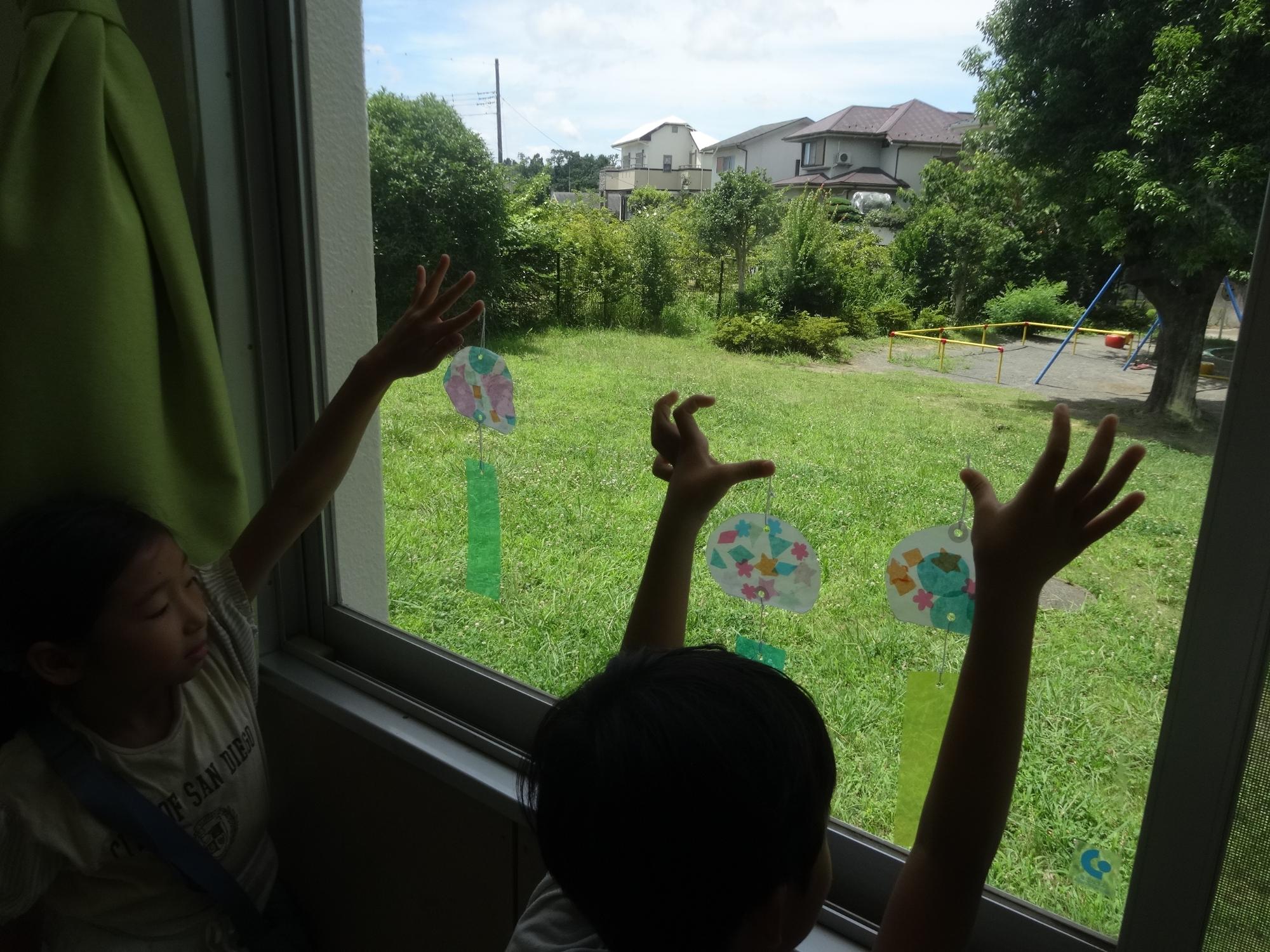 風鈴サンキャッチャーを、窓越しに太陽にかざす子どもたち