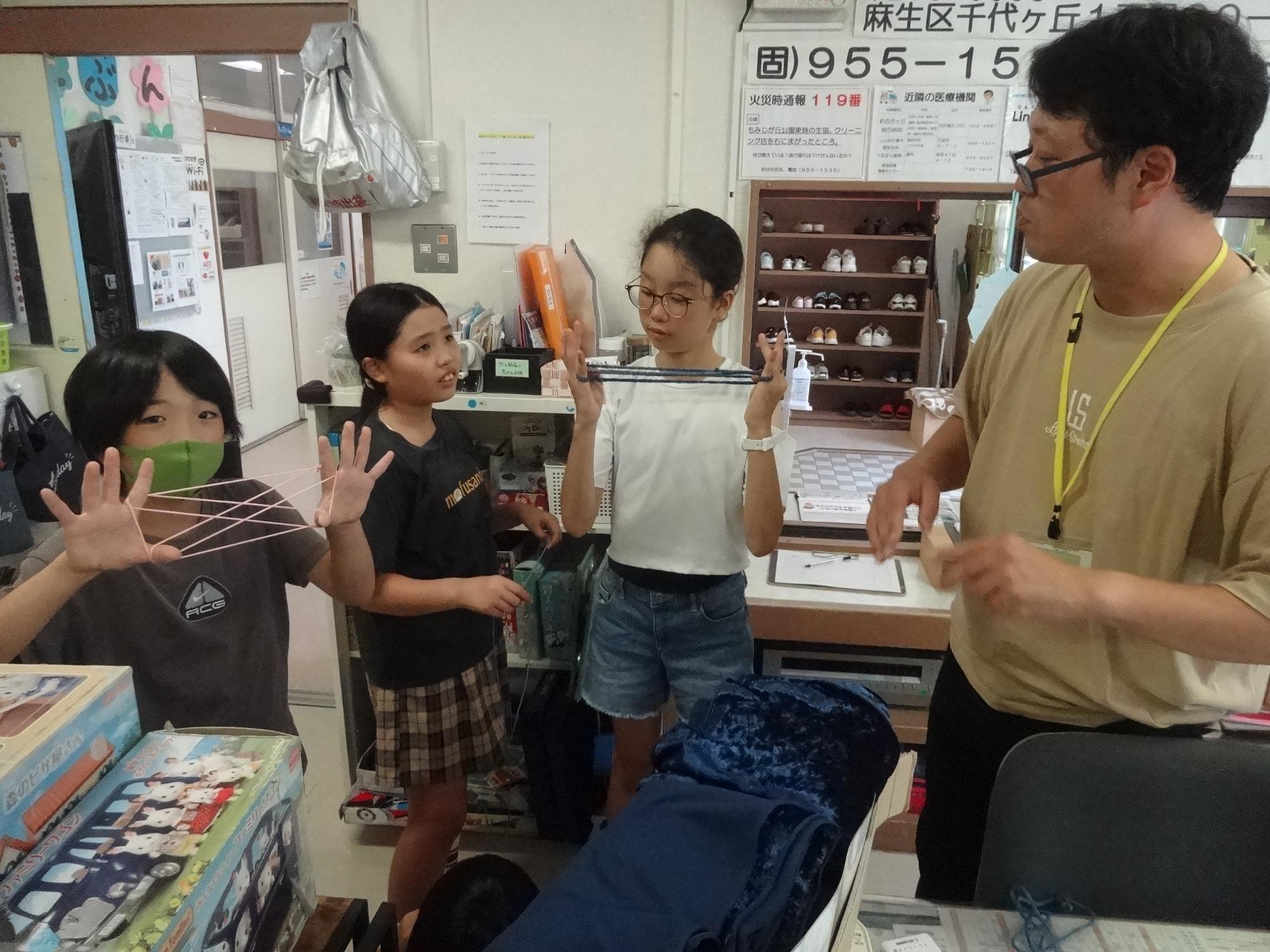 館長と一緒にあやとりをする小学生3人