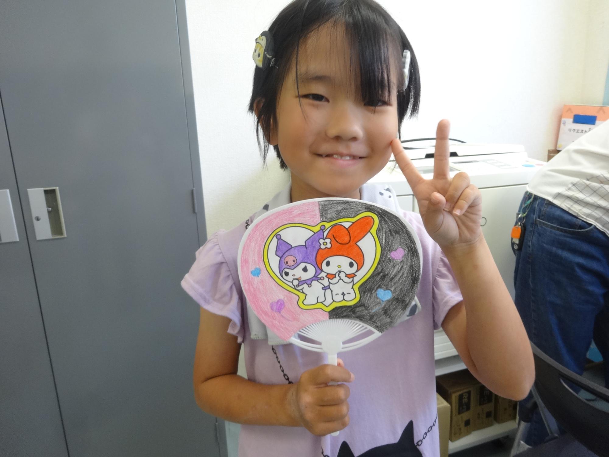 完成したうちわを持ってピースをする小学生女子