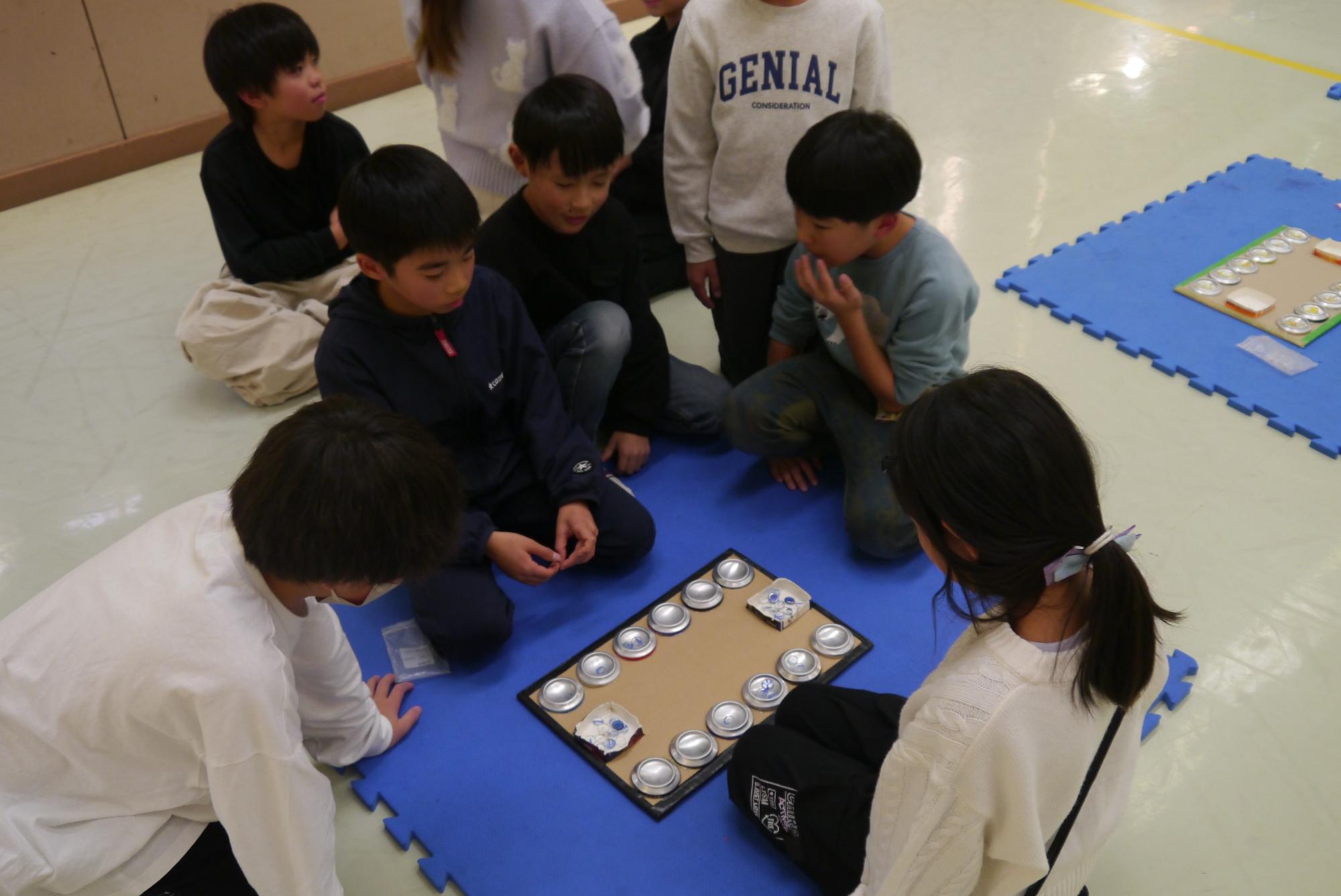 マンカラ対戦をする子どもと見守る子どもたちの写真