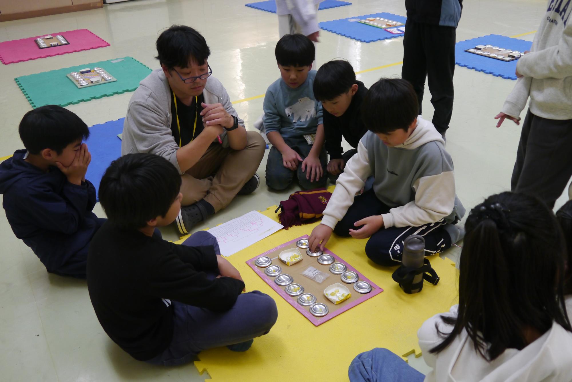 決勝戦を戦う小学生ふたりと、審査をする館長、見守る子どもたちの写真