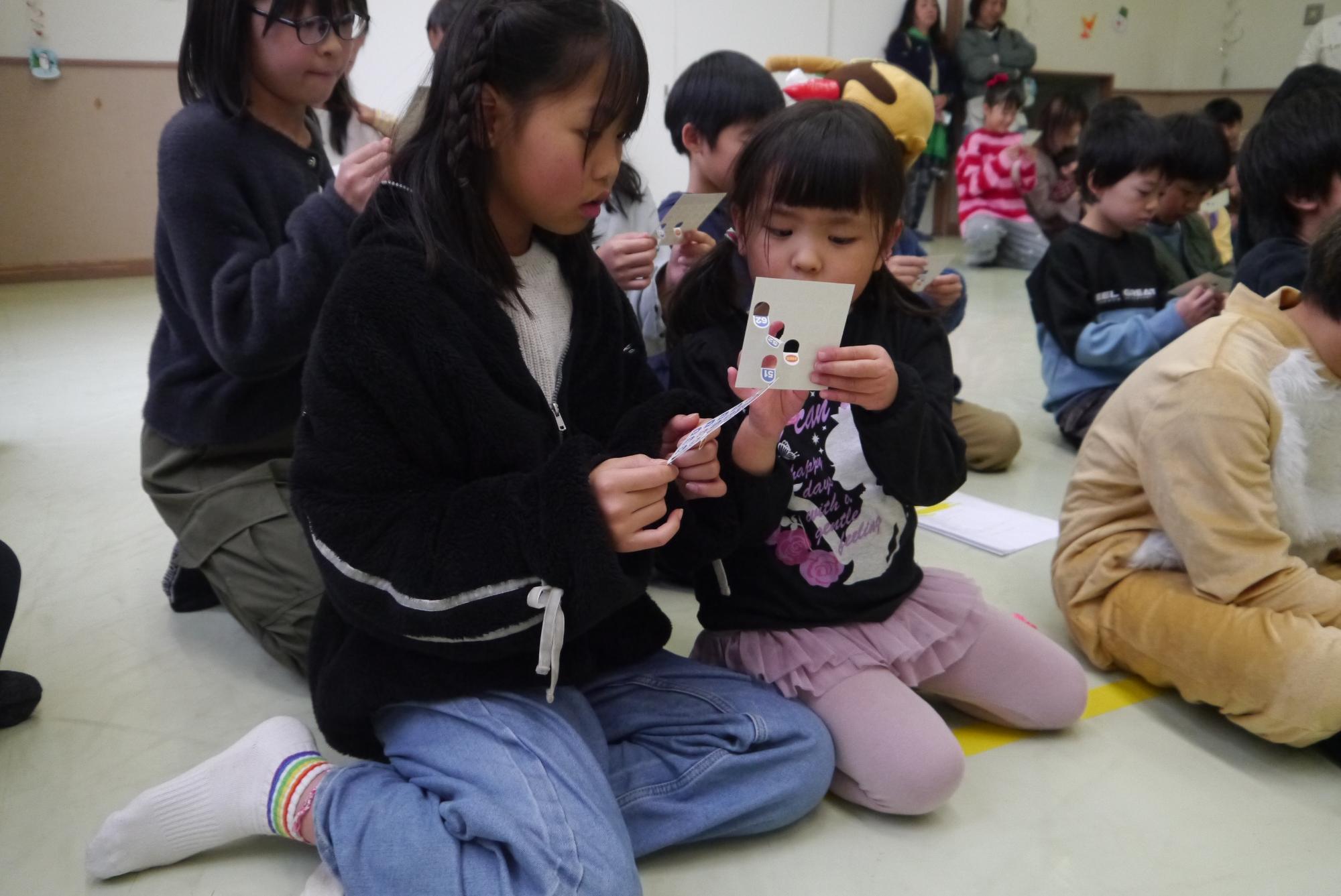 ビンゴ大会でビンゴカードを一生懸命に見ている小学生と幼児