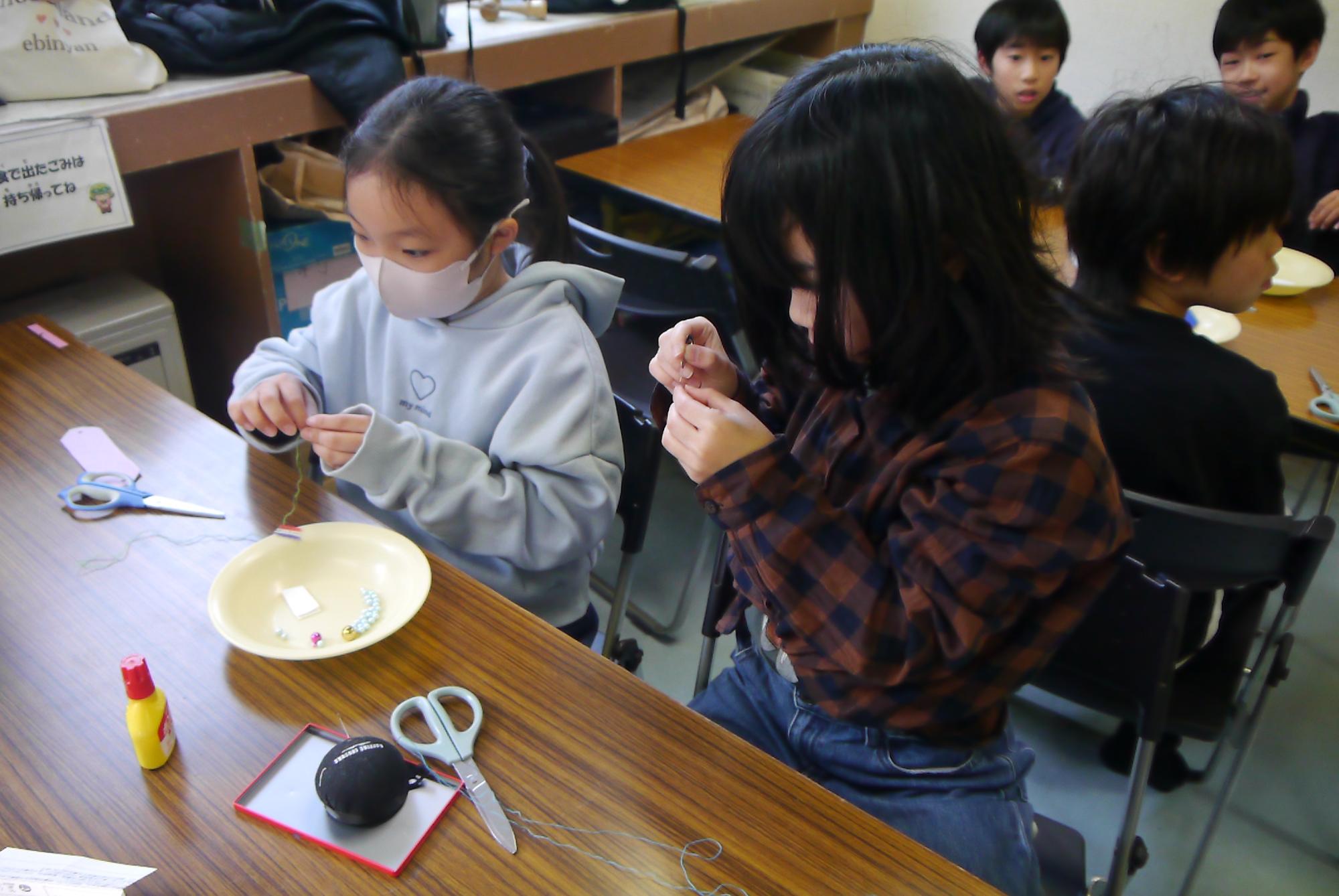 お守りを作るため、針に糸を通す小学生の写真