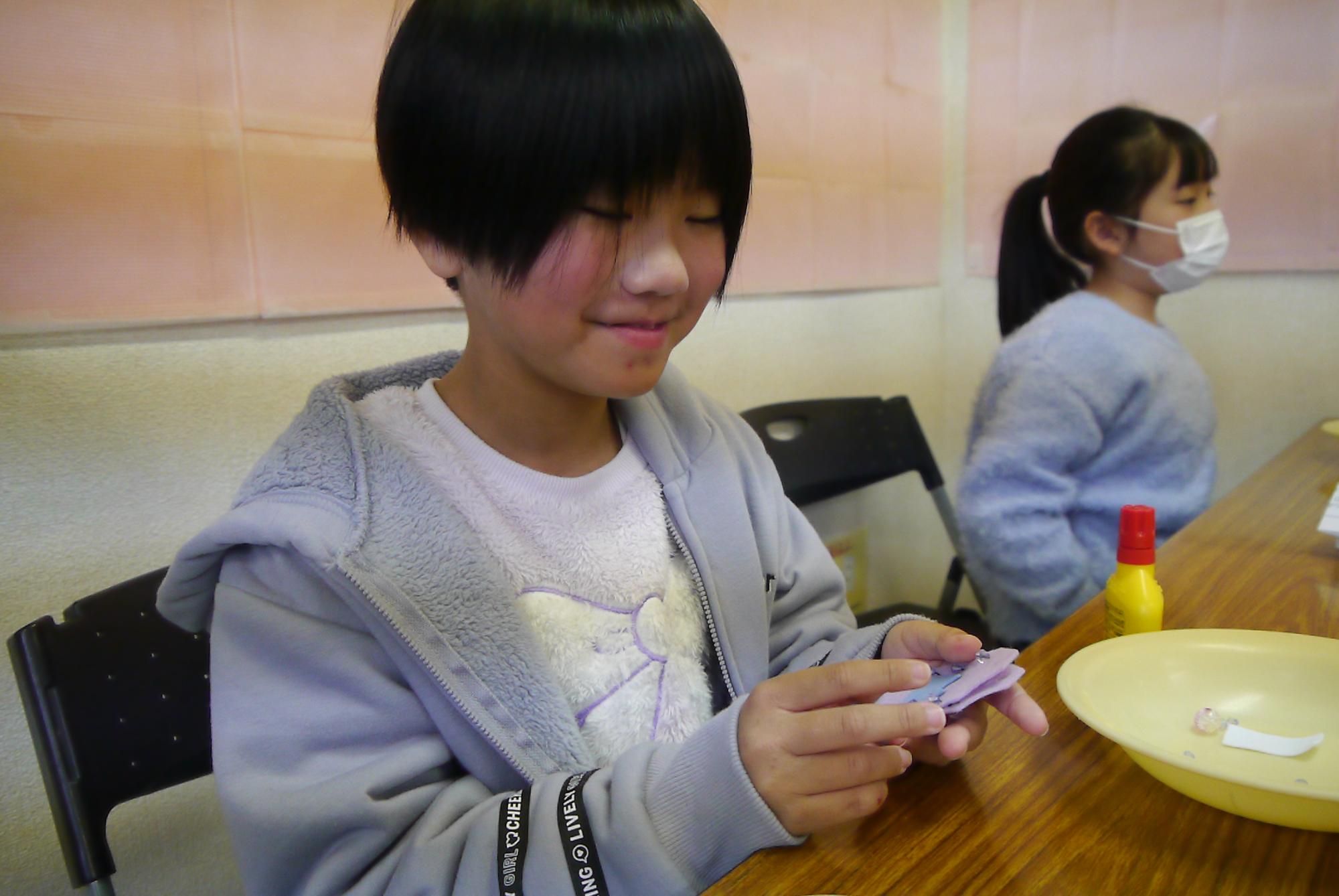 お守りに縫い付けるビーズの位置を考える小学生の写真