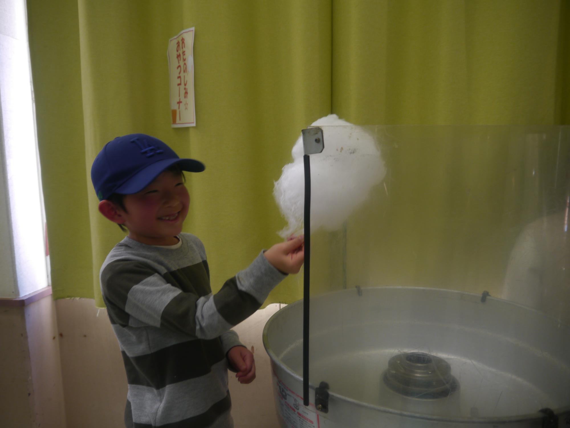 わたあめ作り体験コーナーに挑戦する小学生の写真