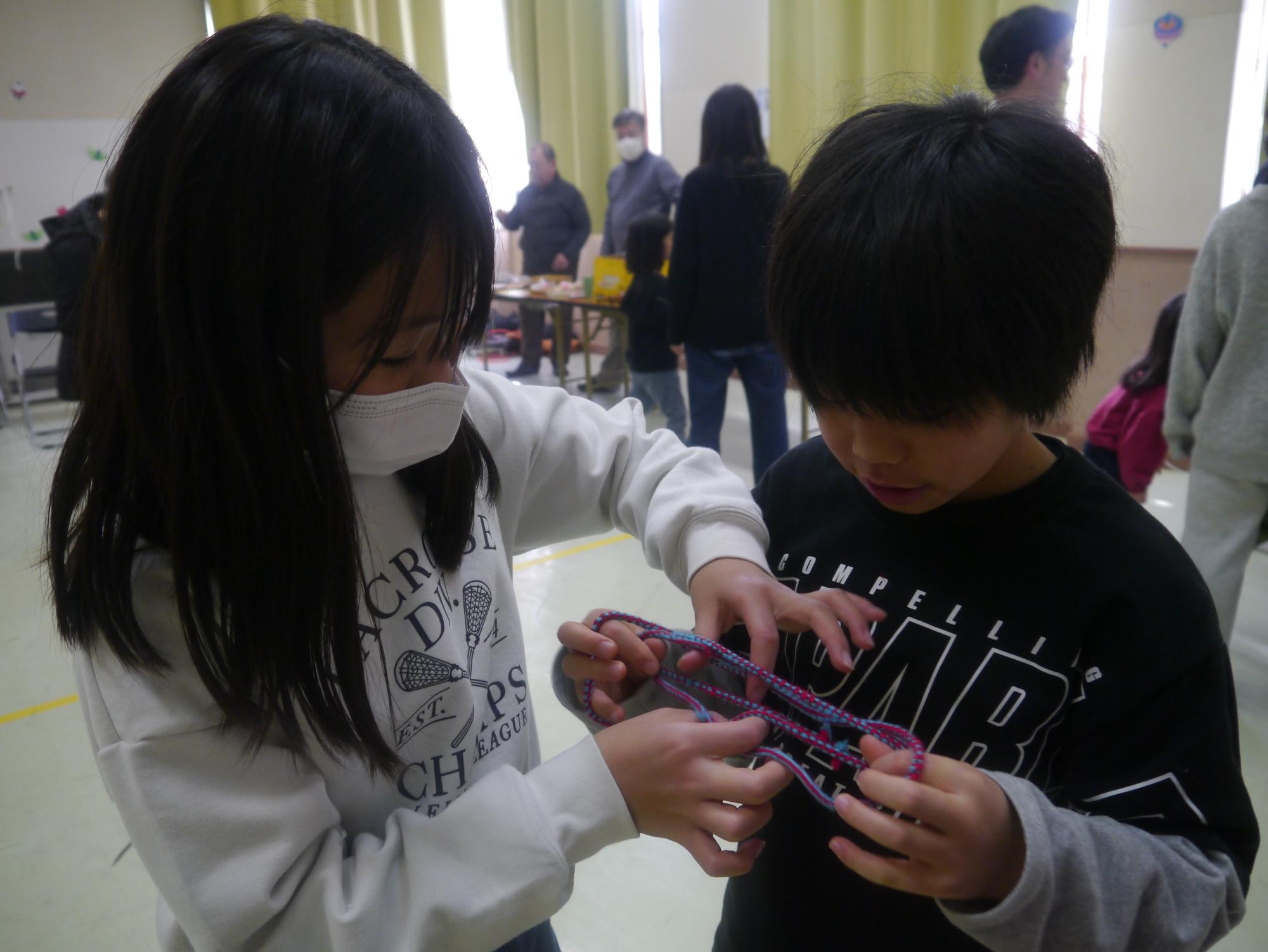 姉弟であやとりに挑戦する小学生の写真