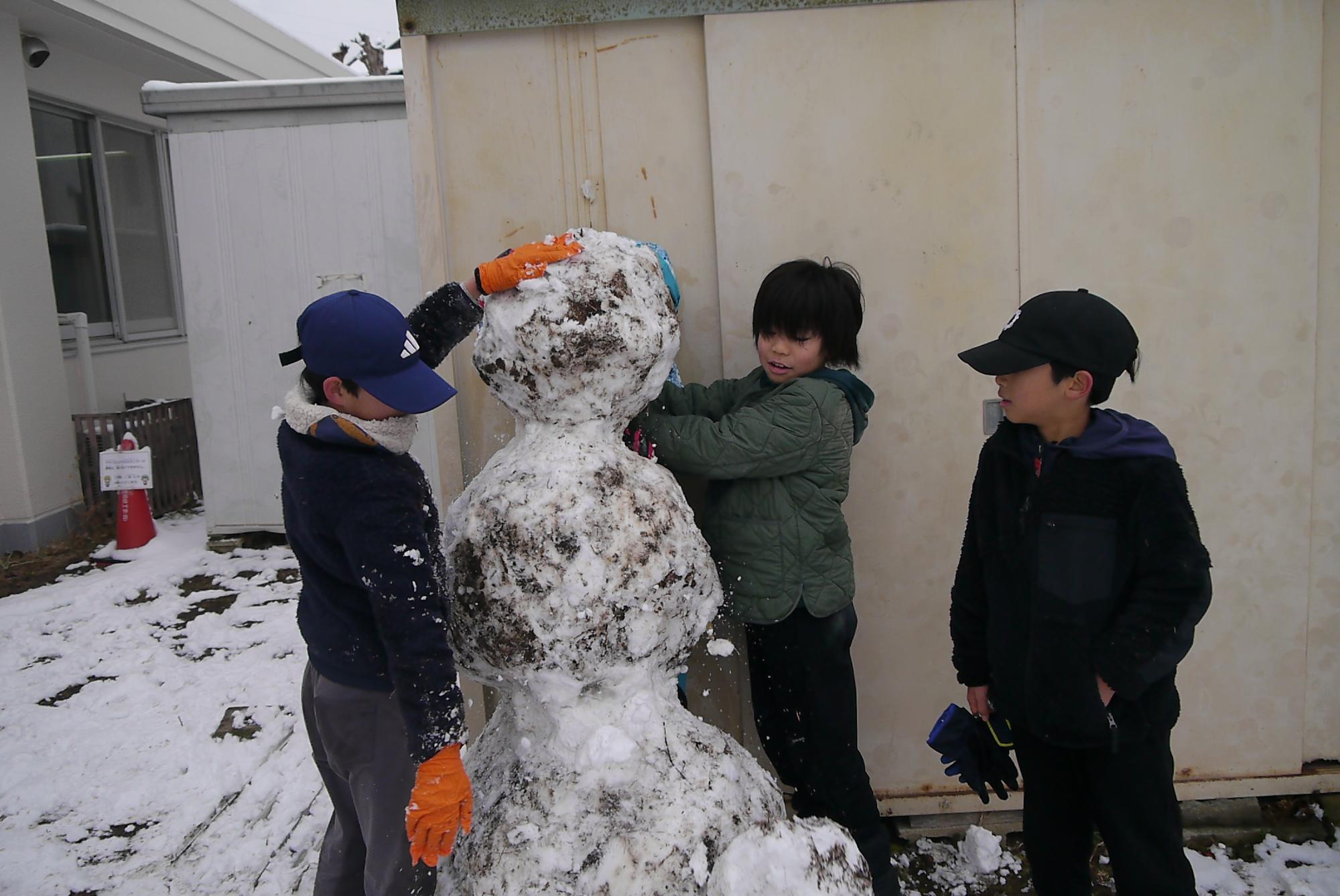 大きな雪だるまを作っている3人の小学生の写真