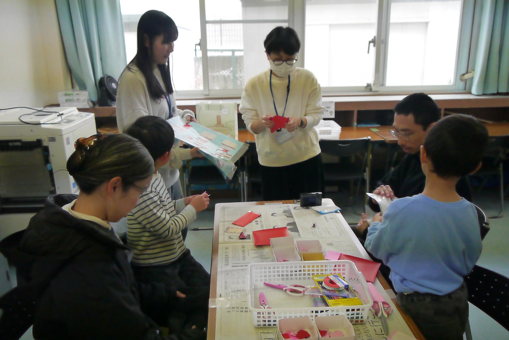 先生から作り方の説明を聞く小学生と幼児親子の写真