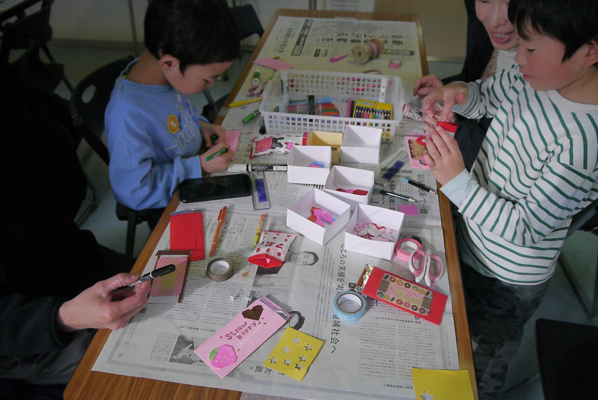 チョコレートの形をしたメッセージカードを作る小学生と幼児