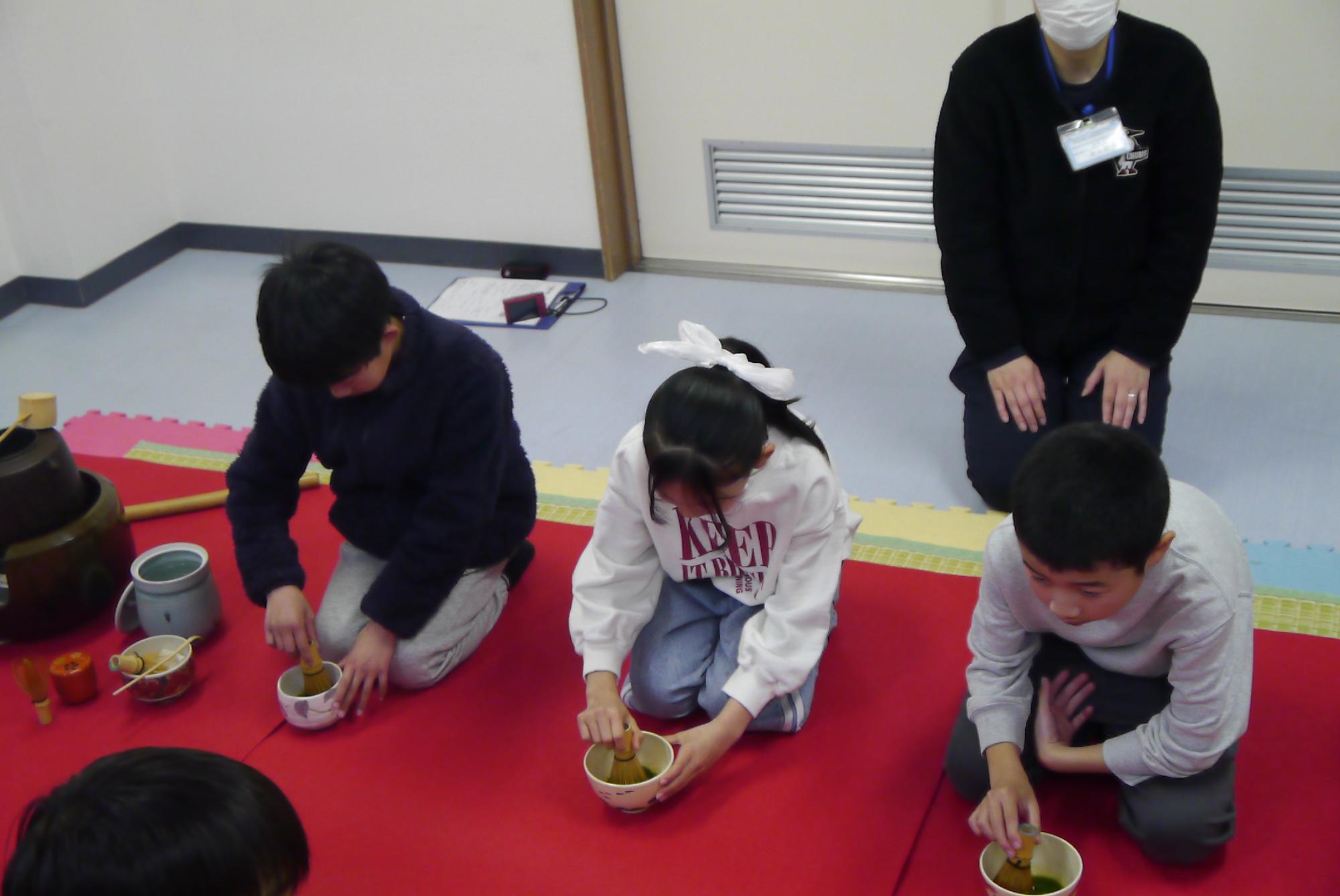 茶筅でお茶をたてる3人の小学生の写真