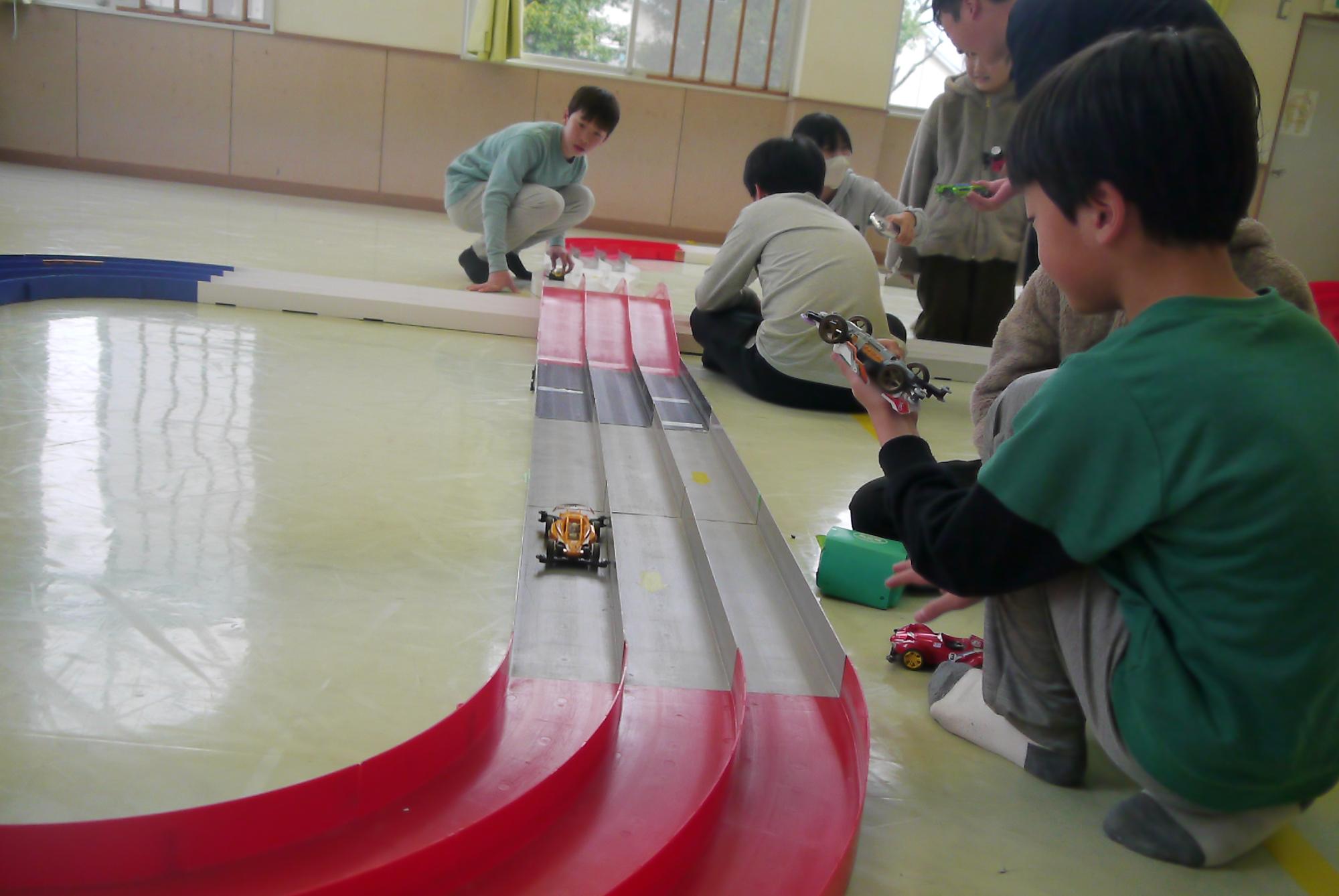 コースを走るミニ四駆の車と子どもたち