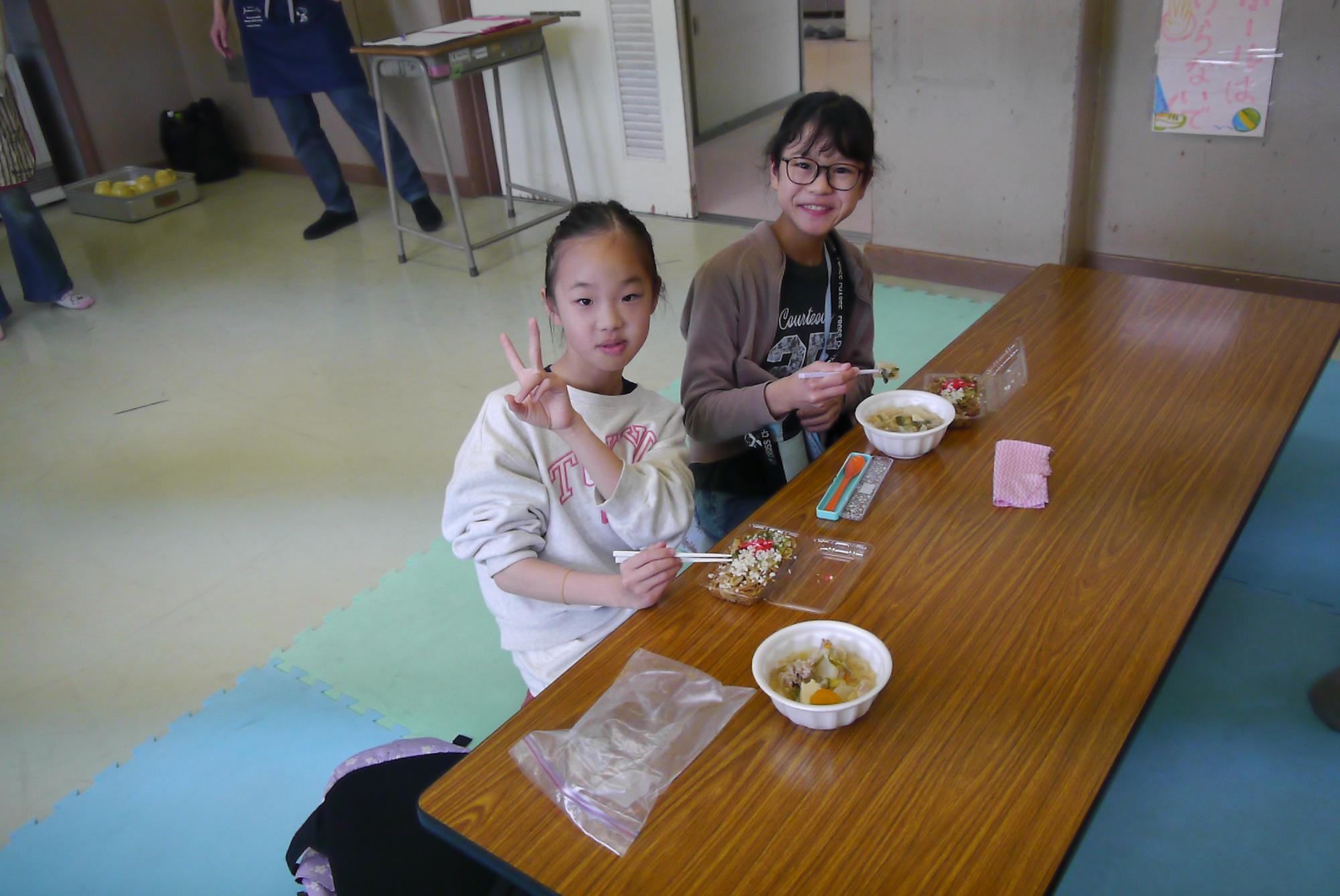 小学生2人が座卓に横並びになって焼きそばと豚汁を食べている写真