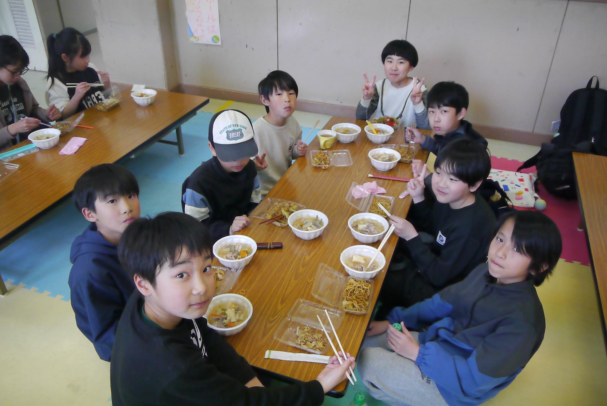 8人の小学生が座卓を囲んで焼きそばと豚汁を食べている写真
