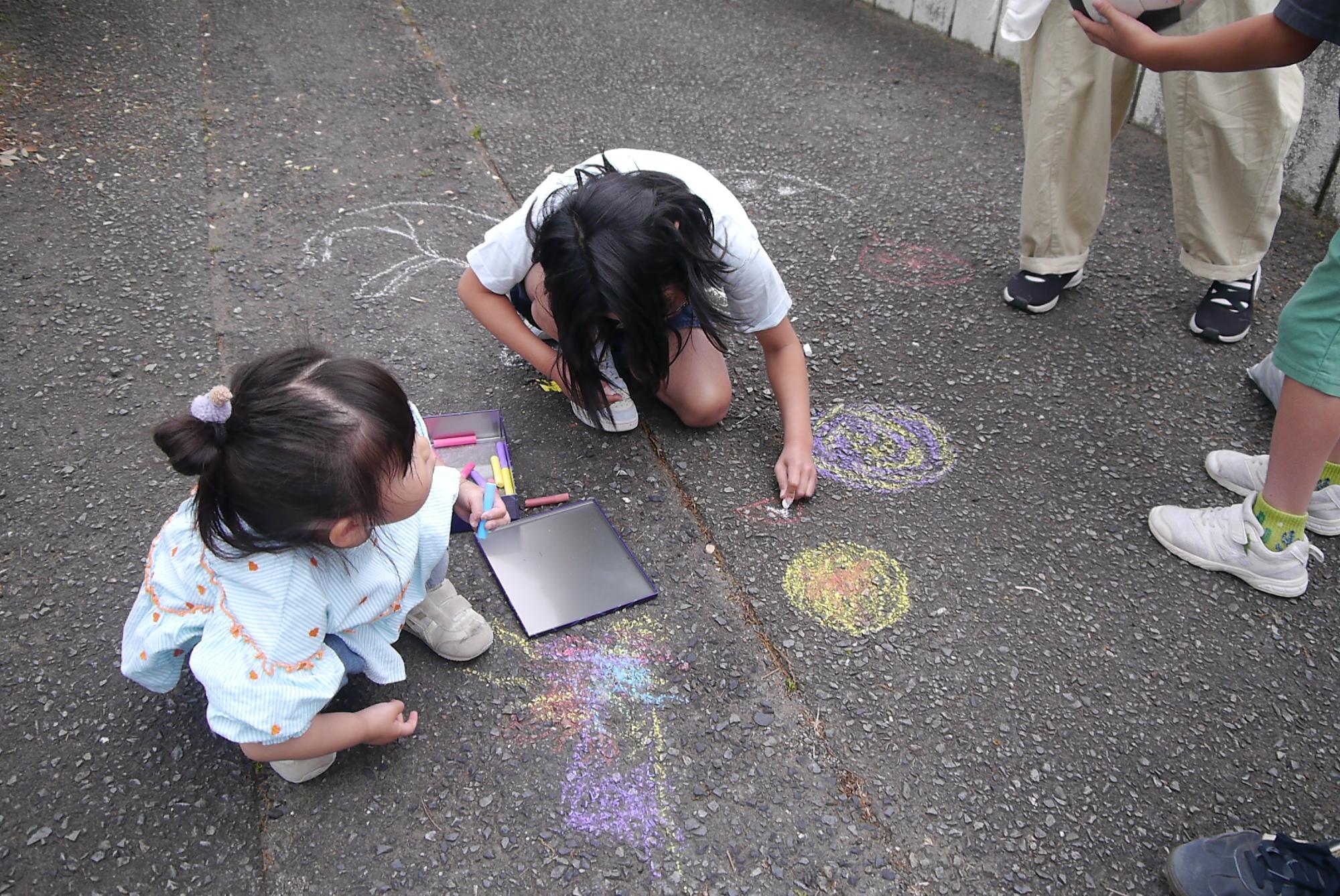 アスファルトにチョークで絵を描くふたりの幼児