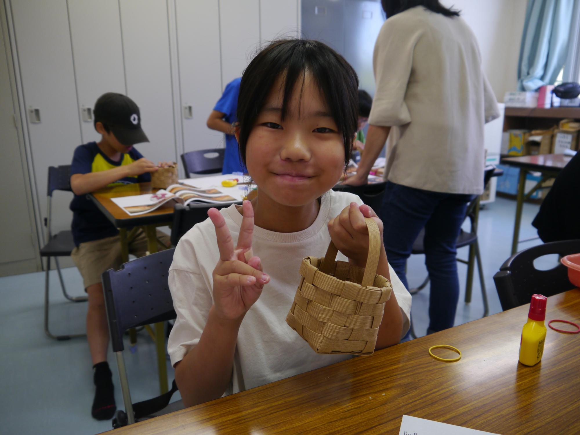 完成したかごを持ってピースサインをする小学生