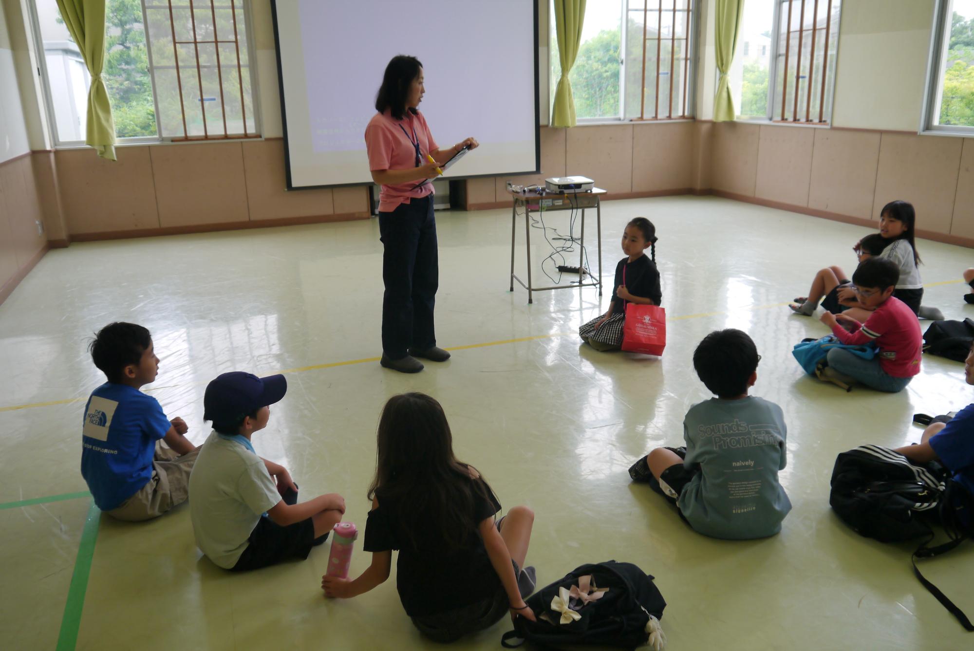 ダンボールハウス作りについて説明する職員と話を聞く子どもたち