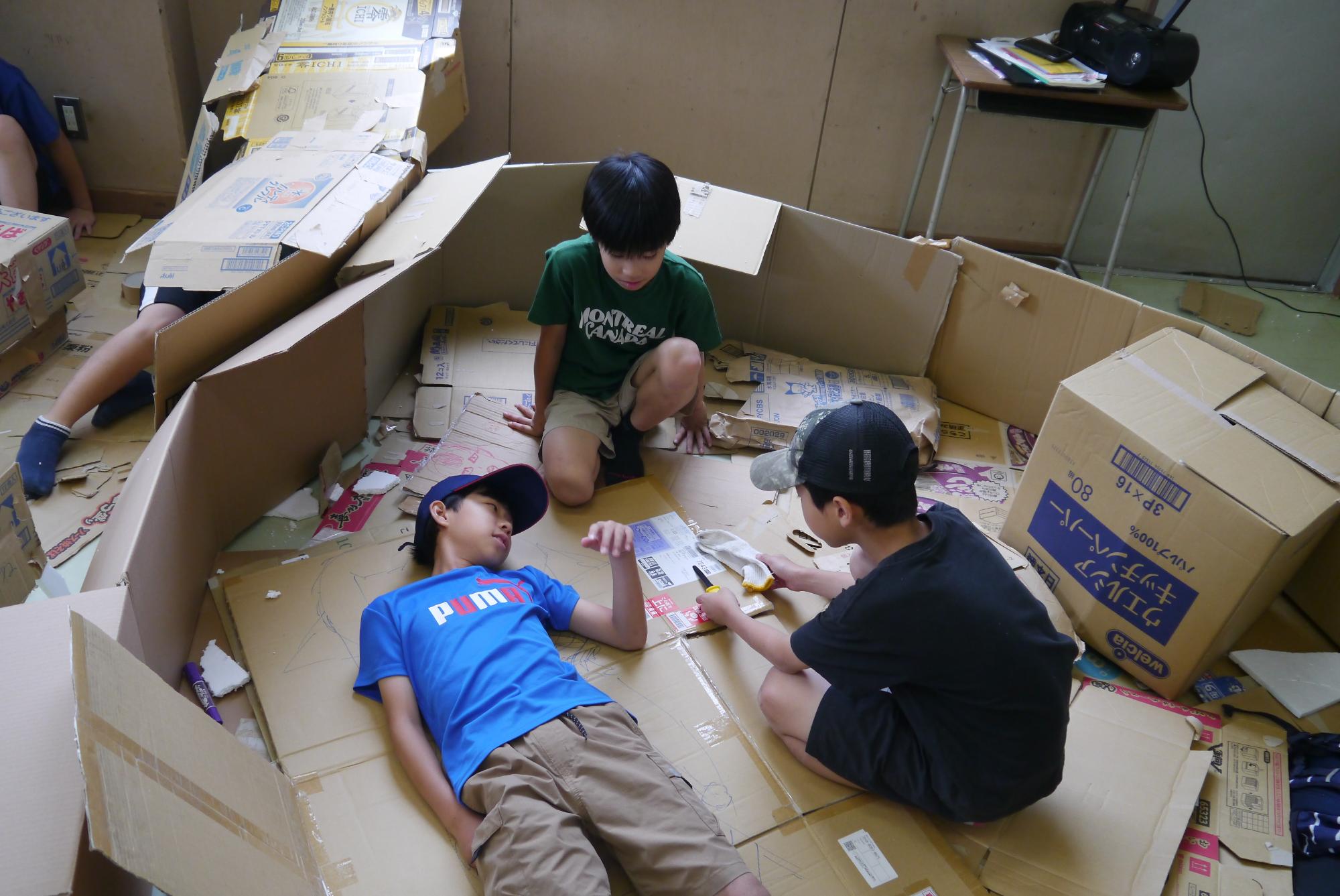 ダンボールハウスの中でくつろぐ小学生男子3人
