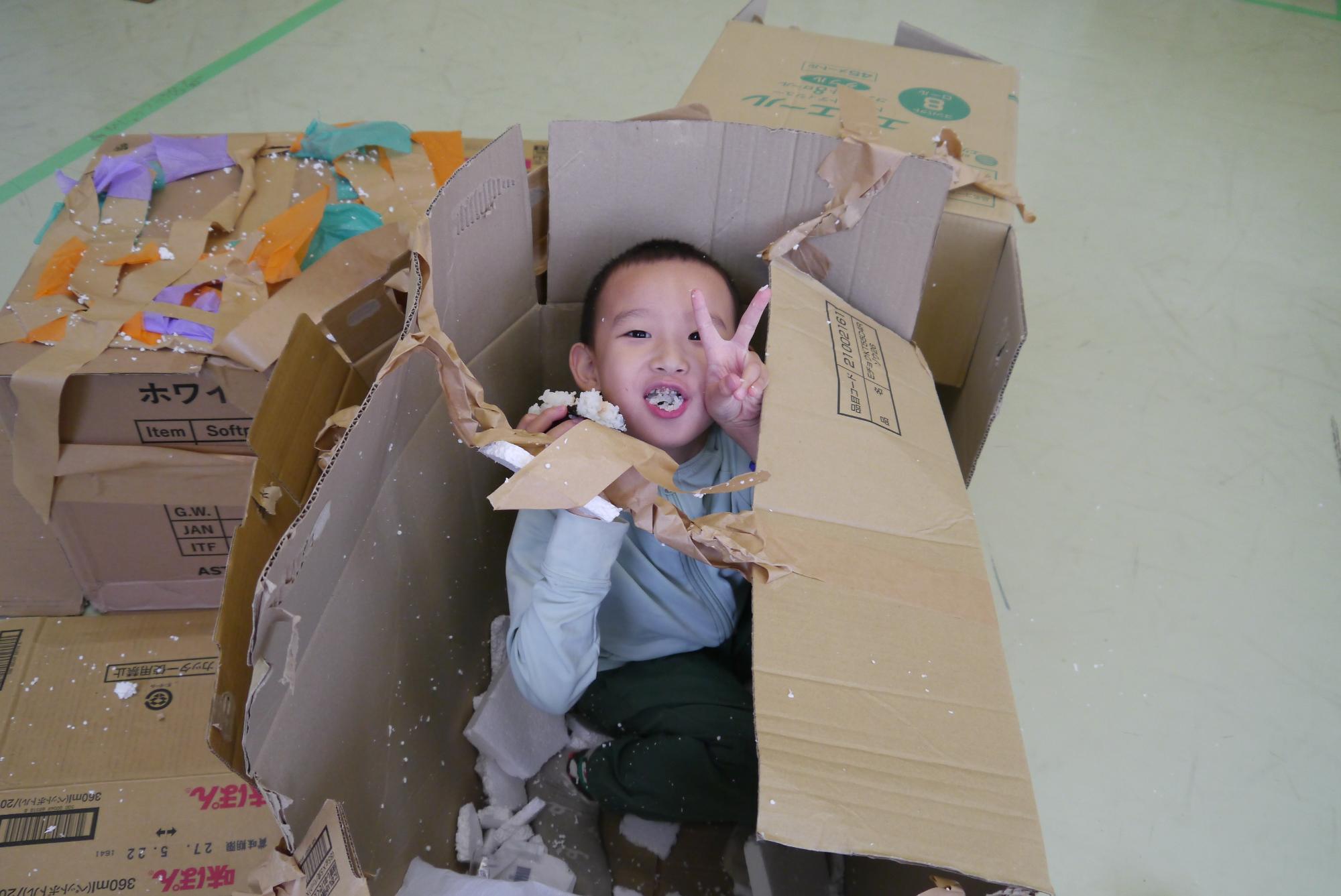 ダンボールハウスの中でお弁当を食べる小学生