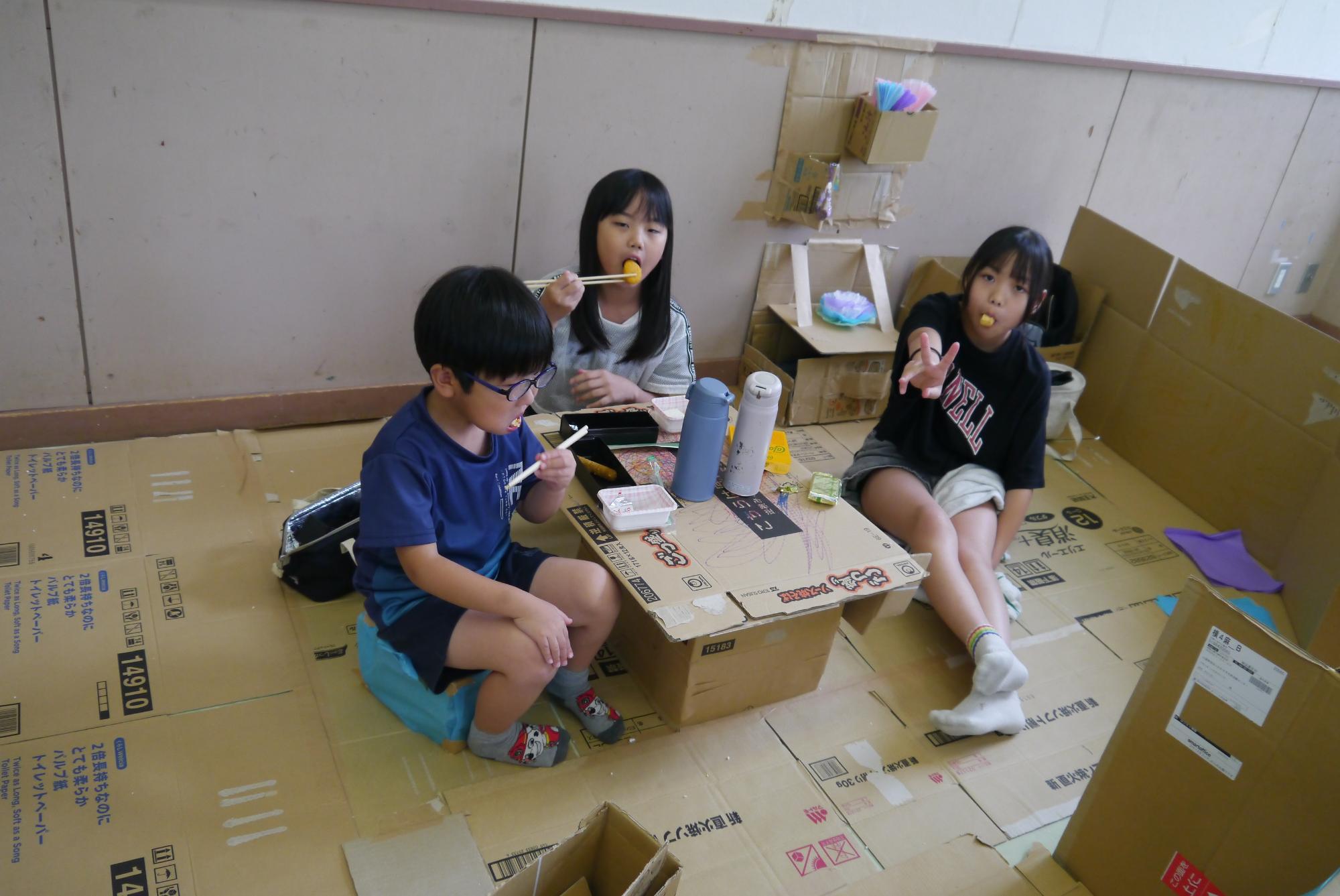 ダンボールハウスの中でお弁当を食べる小学生