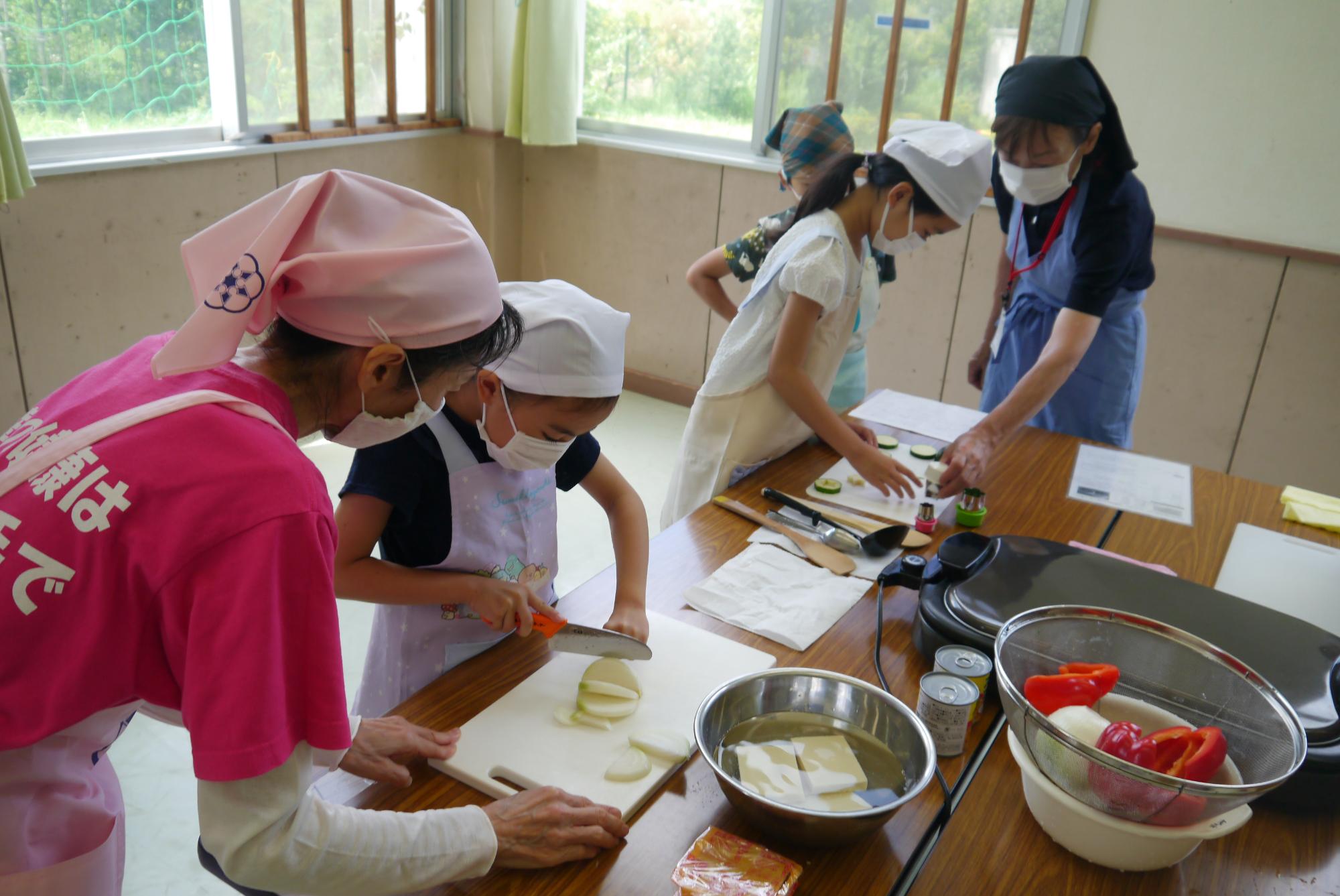 野菜を切る小学生と見守るボランティア