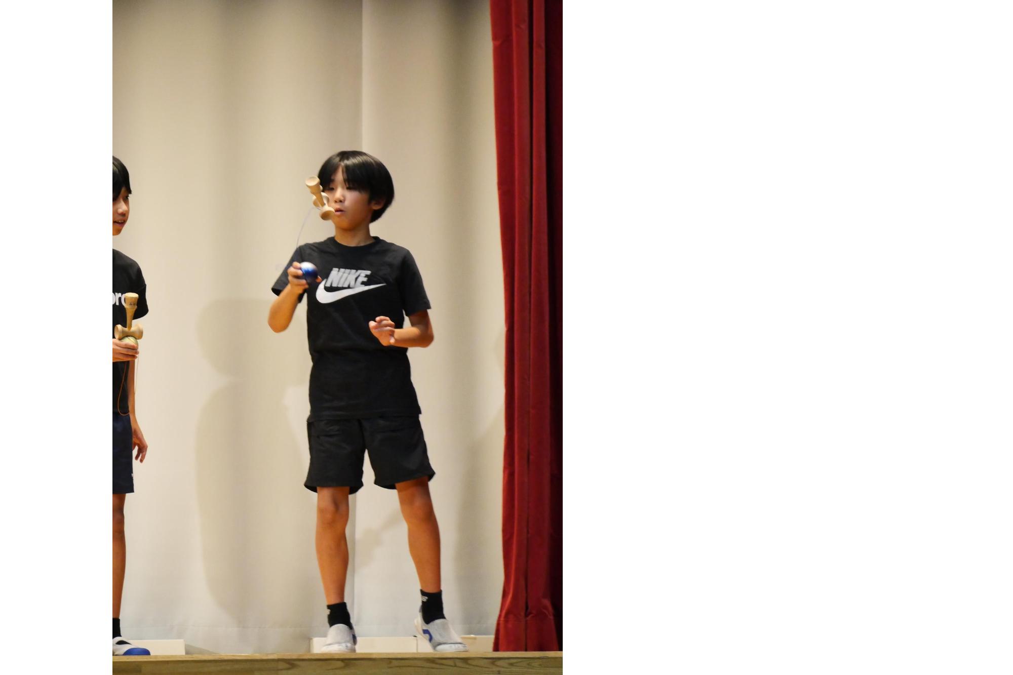 けん玉の球を持ち、けん玉本体を振り上げて穴に剣先を入れようとしている小学生の写真