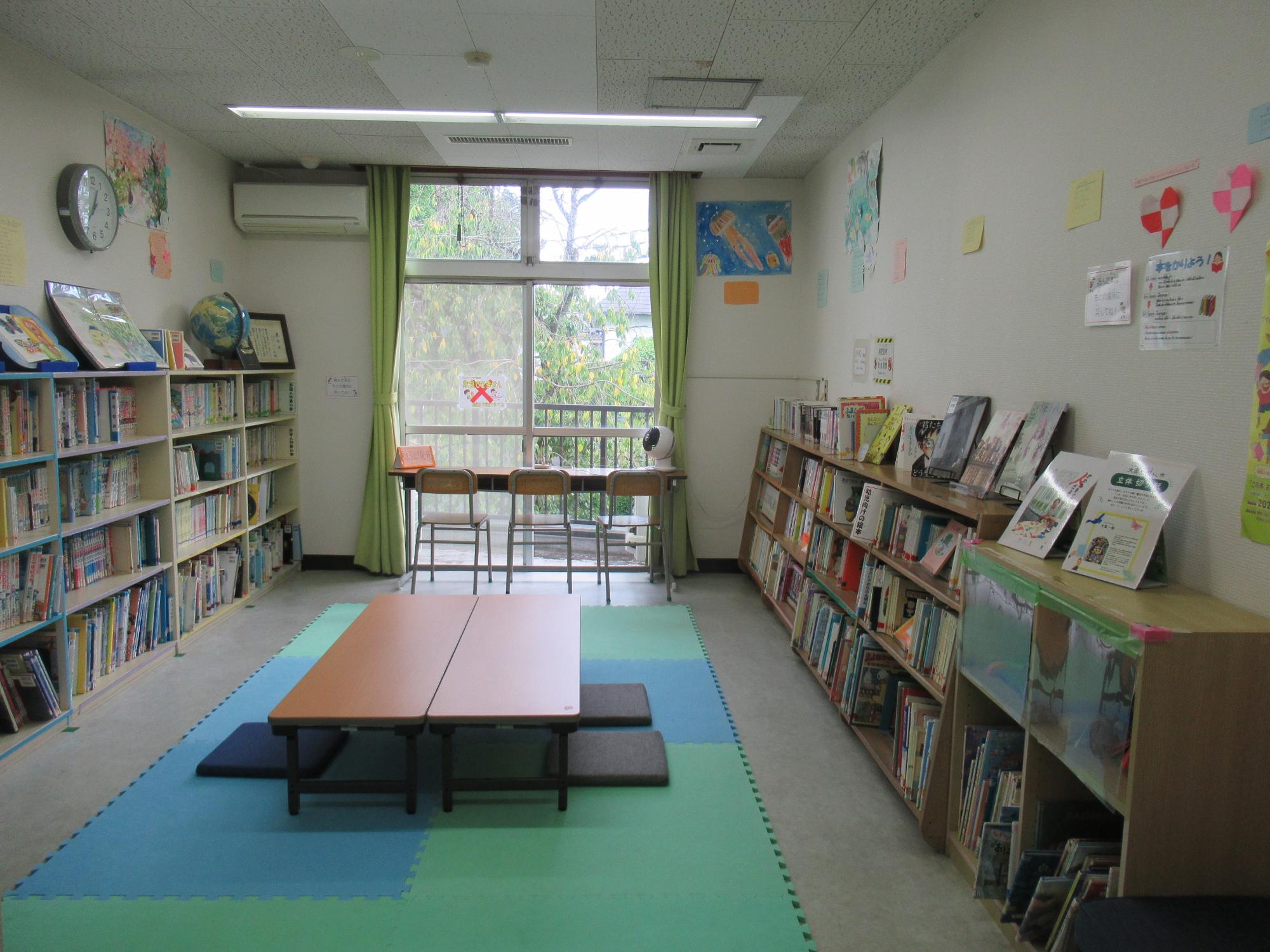 本棚に沢山の本が並べられ、長机が置かれた図書室の写真