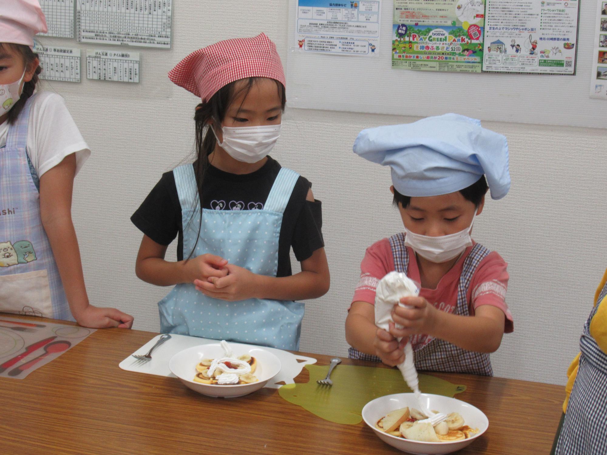 子どもがパンケーキにホイップクリームを搾っている写真