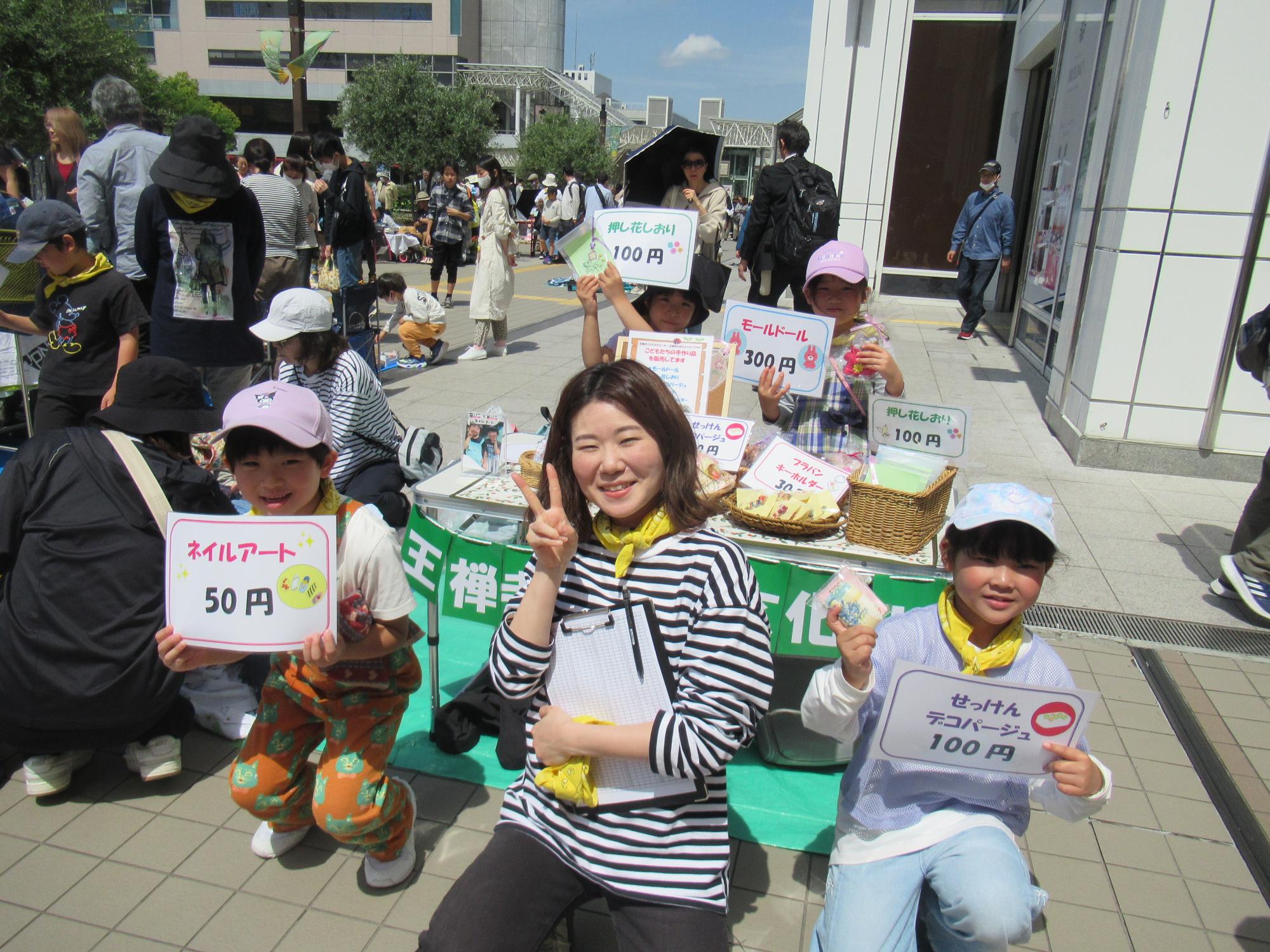 フリーマーケットで販売ブースの前でポーズをとる子ども達と職員の写真