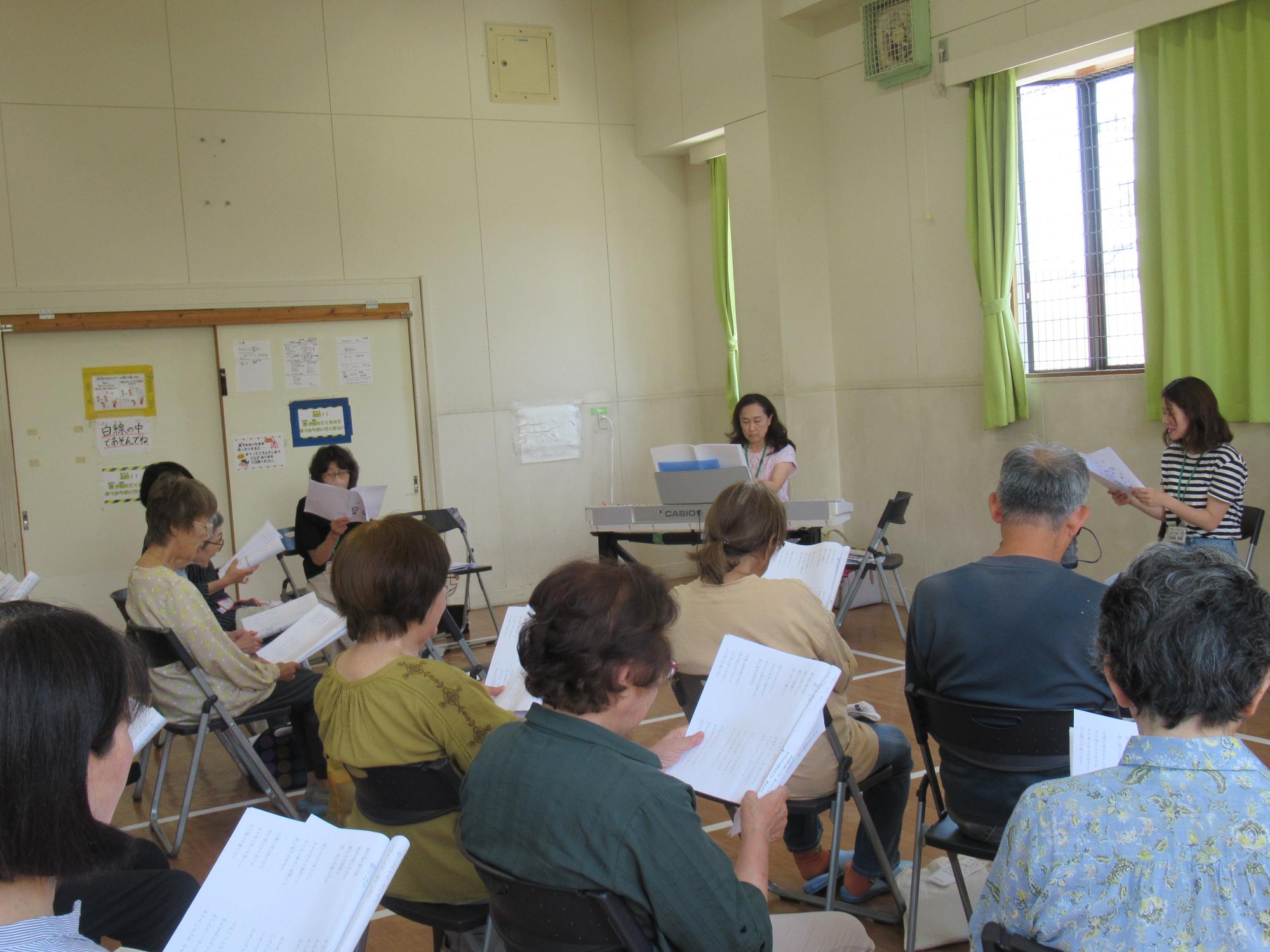 参加者が講師のピアノの演奏に合わせて歌詞カードを見ながら歌を歌っている写真