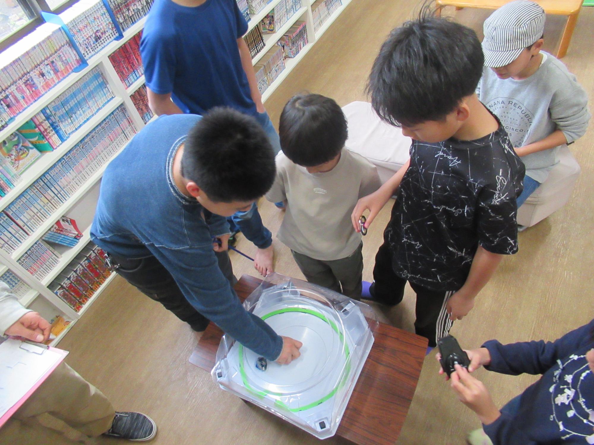 小学生にベイブレードを教えている中学生の写真