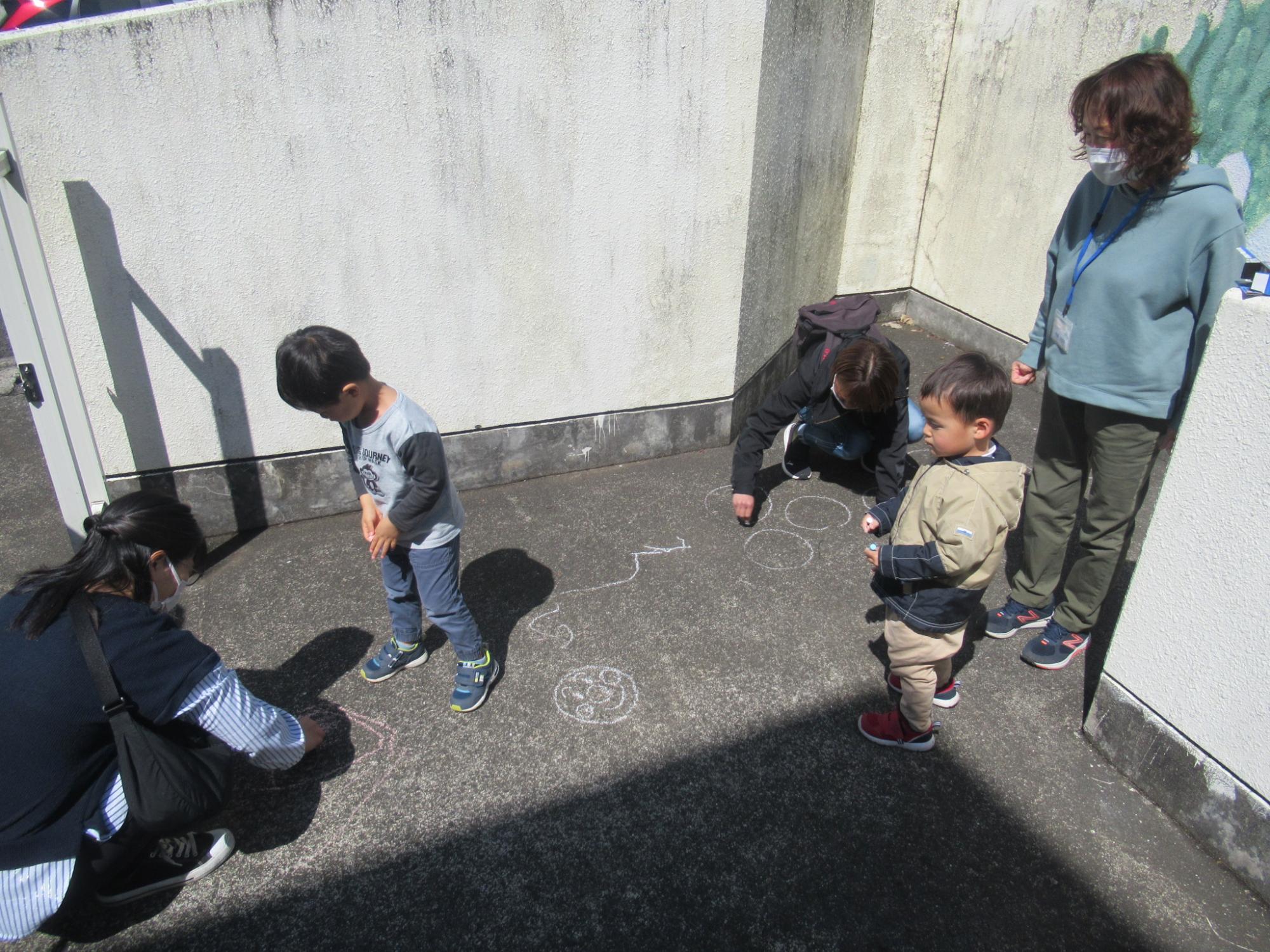 地面にチョークでお絵描きをしている幼児の写真