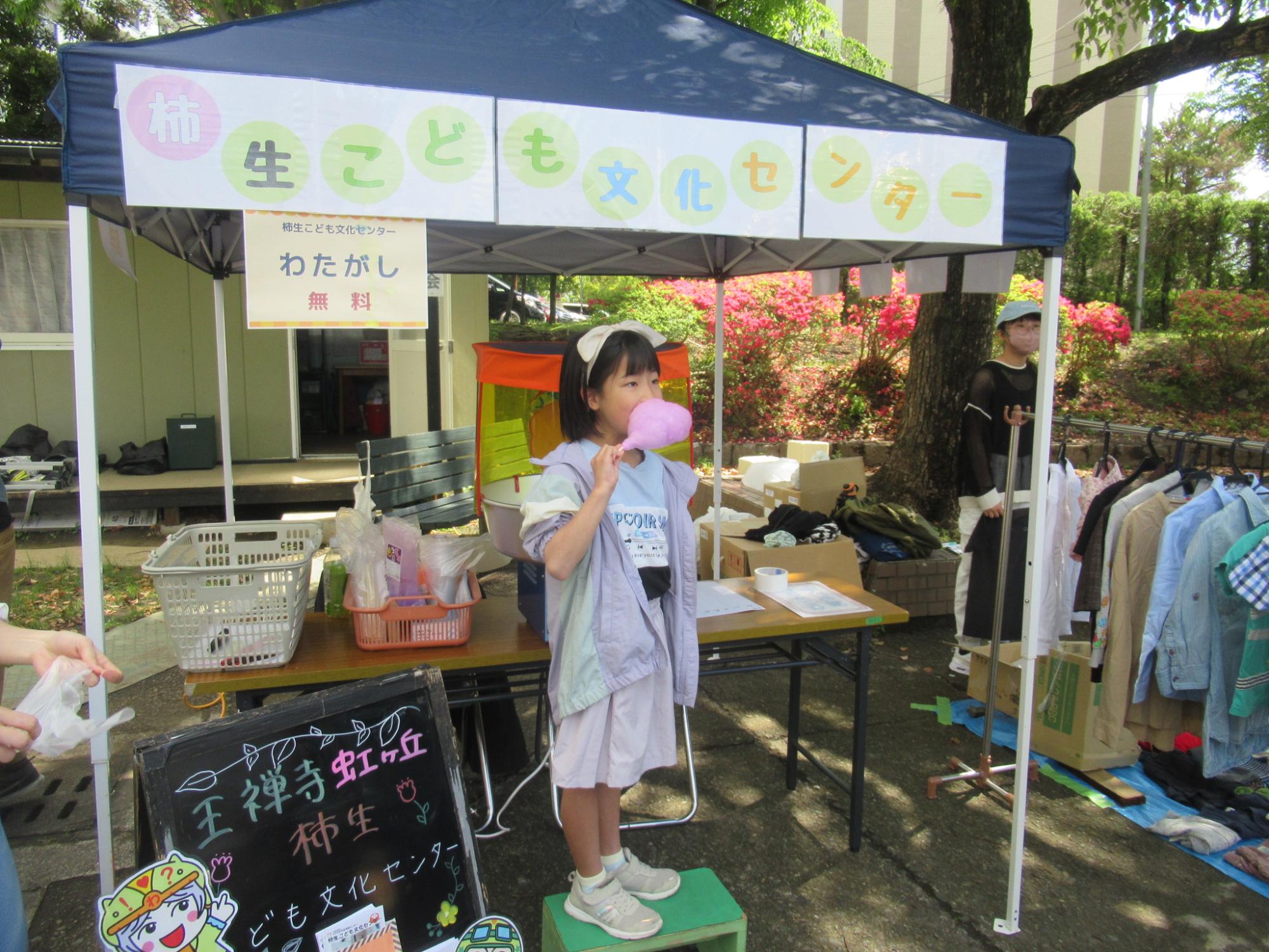 台の上に載ってわたあめを食べている小学生の写真