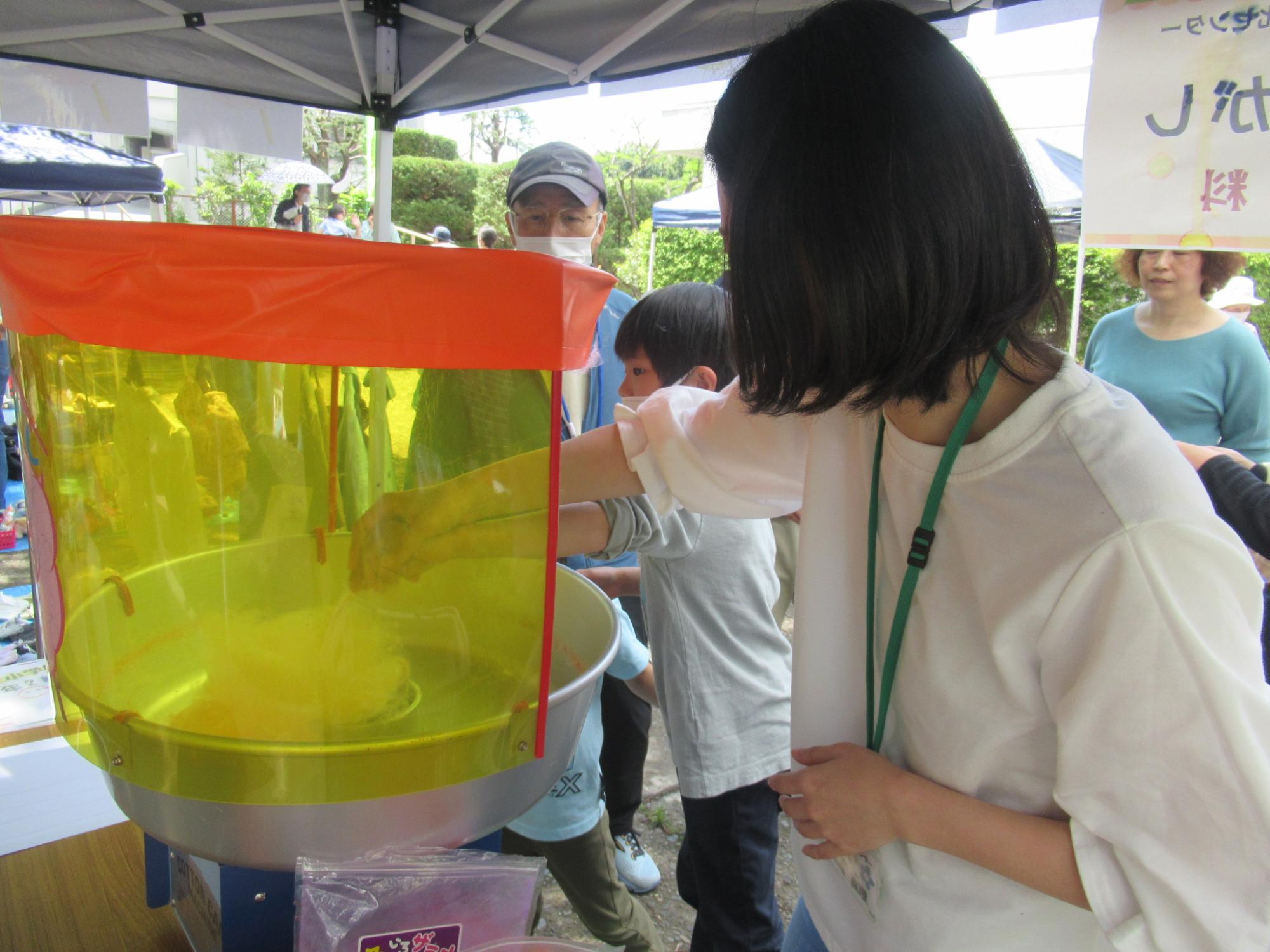 大人と一緒に綿あめを作っている子どもの写真