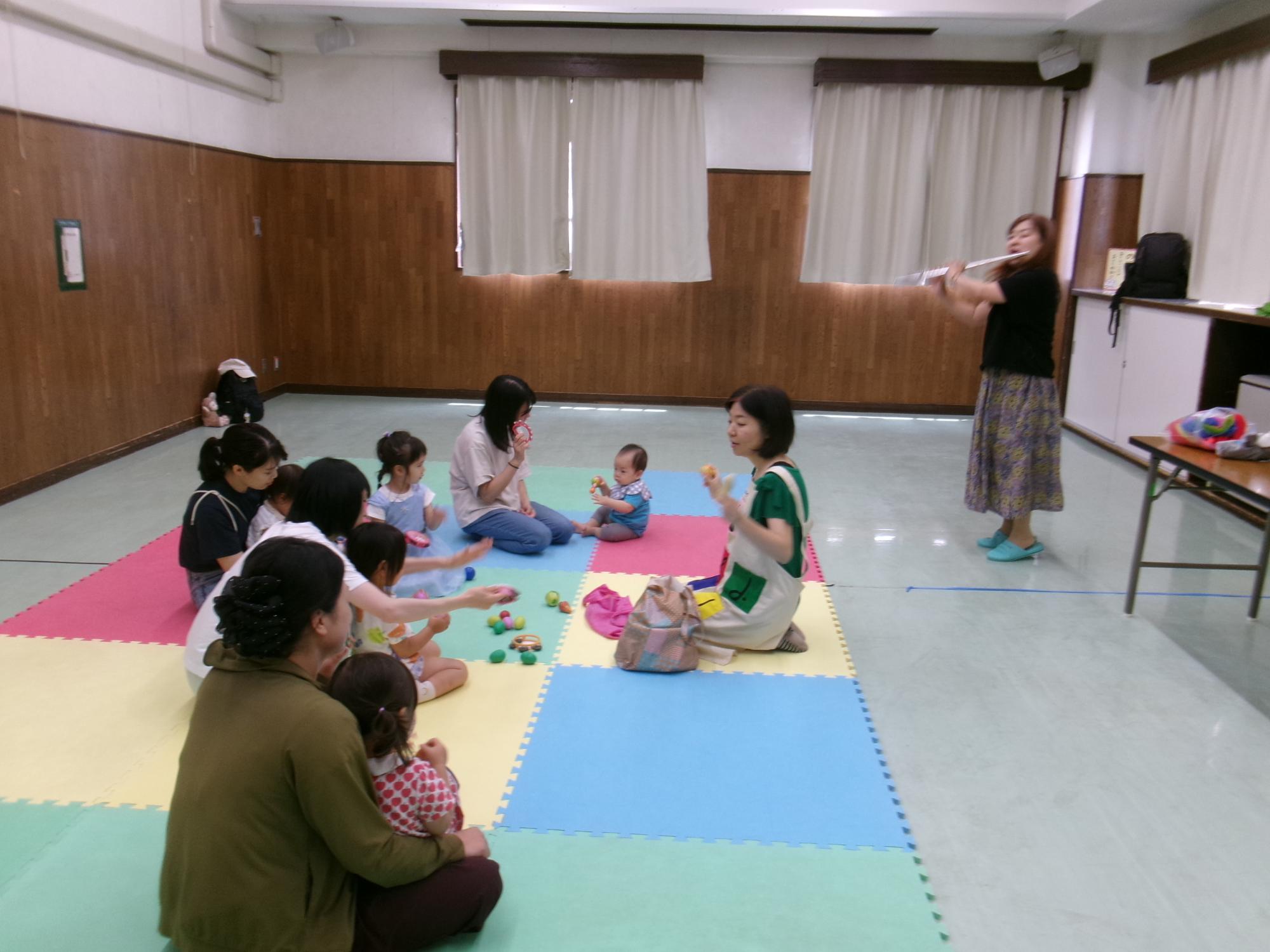 ベビーマッサージ＆リトミックで楽器を演奏する講師と参加した乳幼児親子の写真
