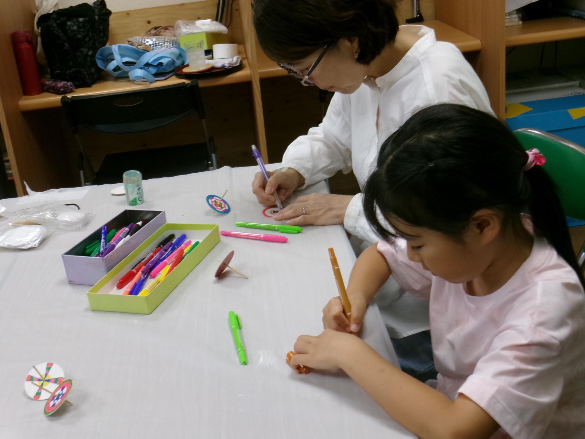 コマの台紙に色を塗る小学生児童とその保護者の写真