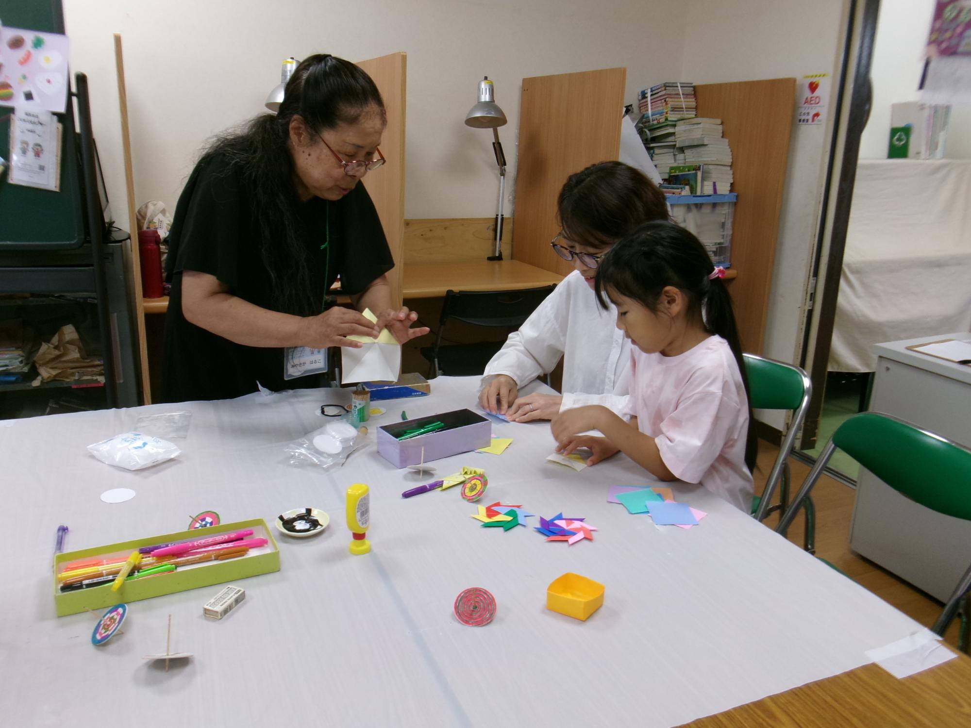 講師にコマの作り方を教わる小学生児童とその保護者の写真
