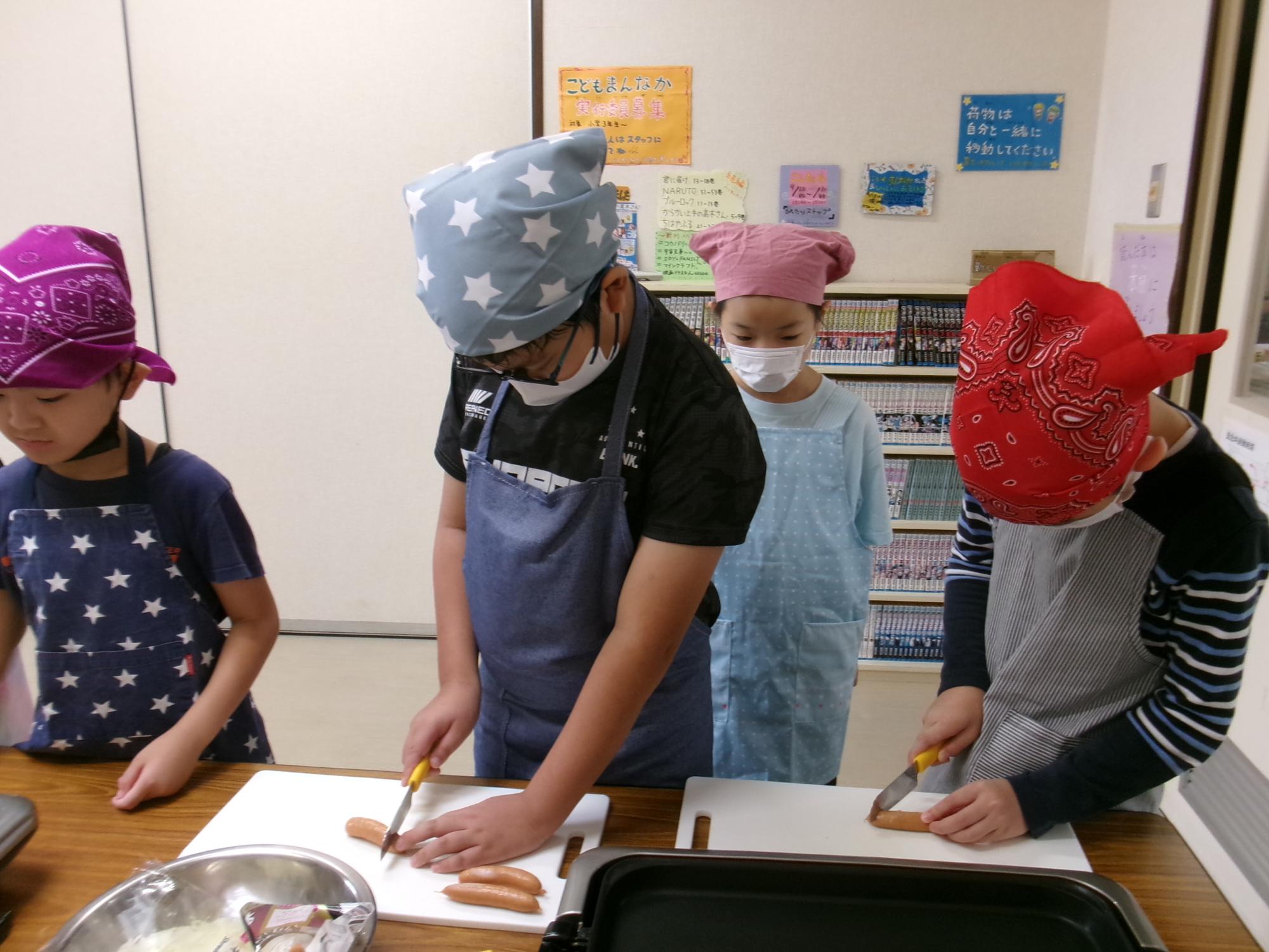 包丁を使ってソーセージを切る小学生児童の様子の写真